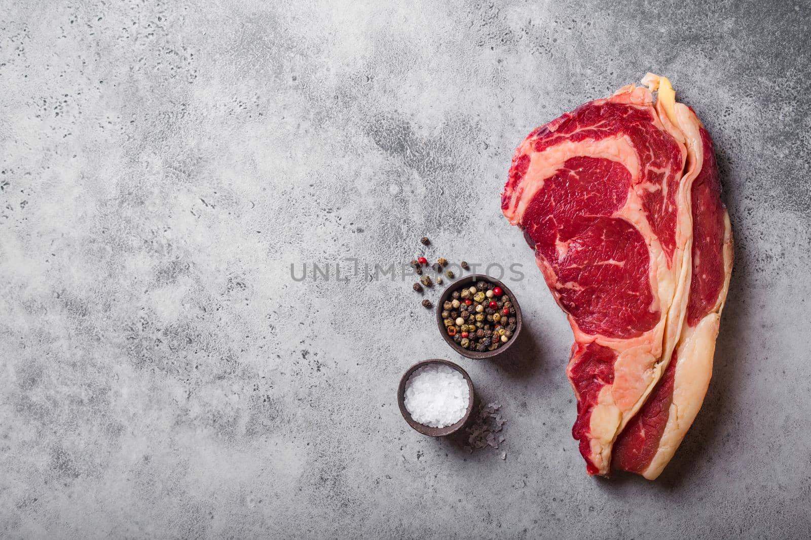 Top view of raw marbled juicy meat beef Rib eye steak ready for cooking, with seasonings, grey concrete rustic background, space for text