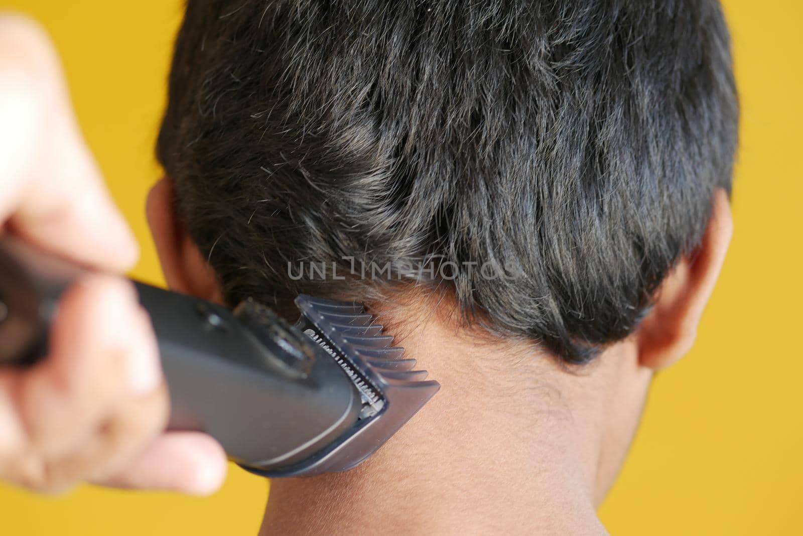 cutting hair with a hair-clipper on yellow background .