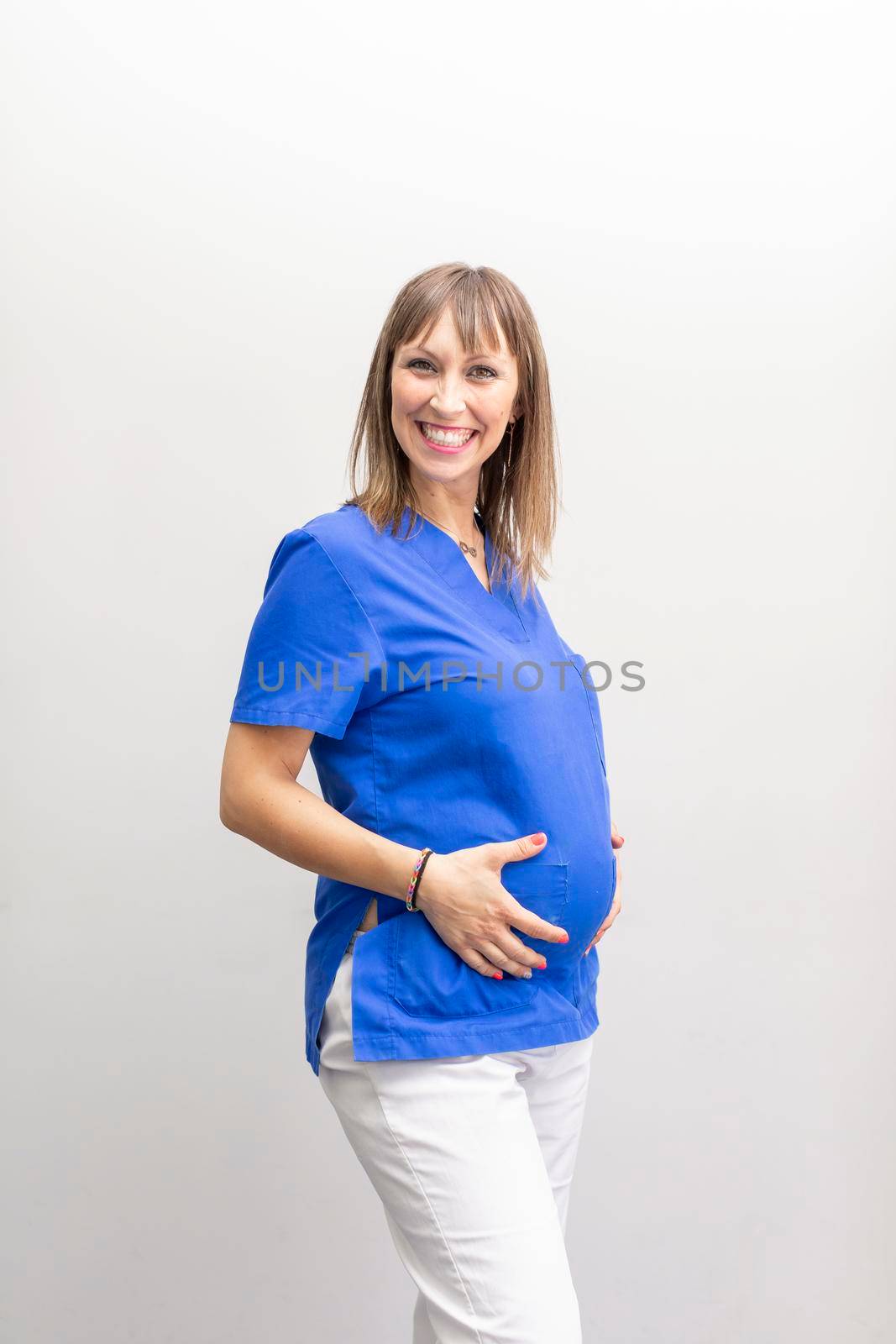 Portrait of a dentist woman, touching her pregnant belly at the dental clinic by stockrojoverdeyazul