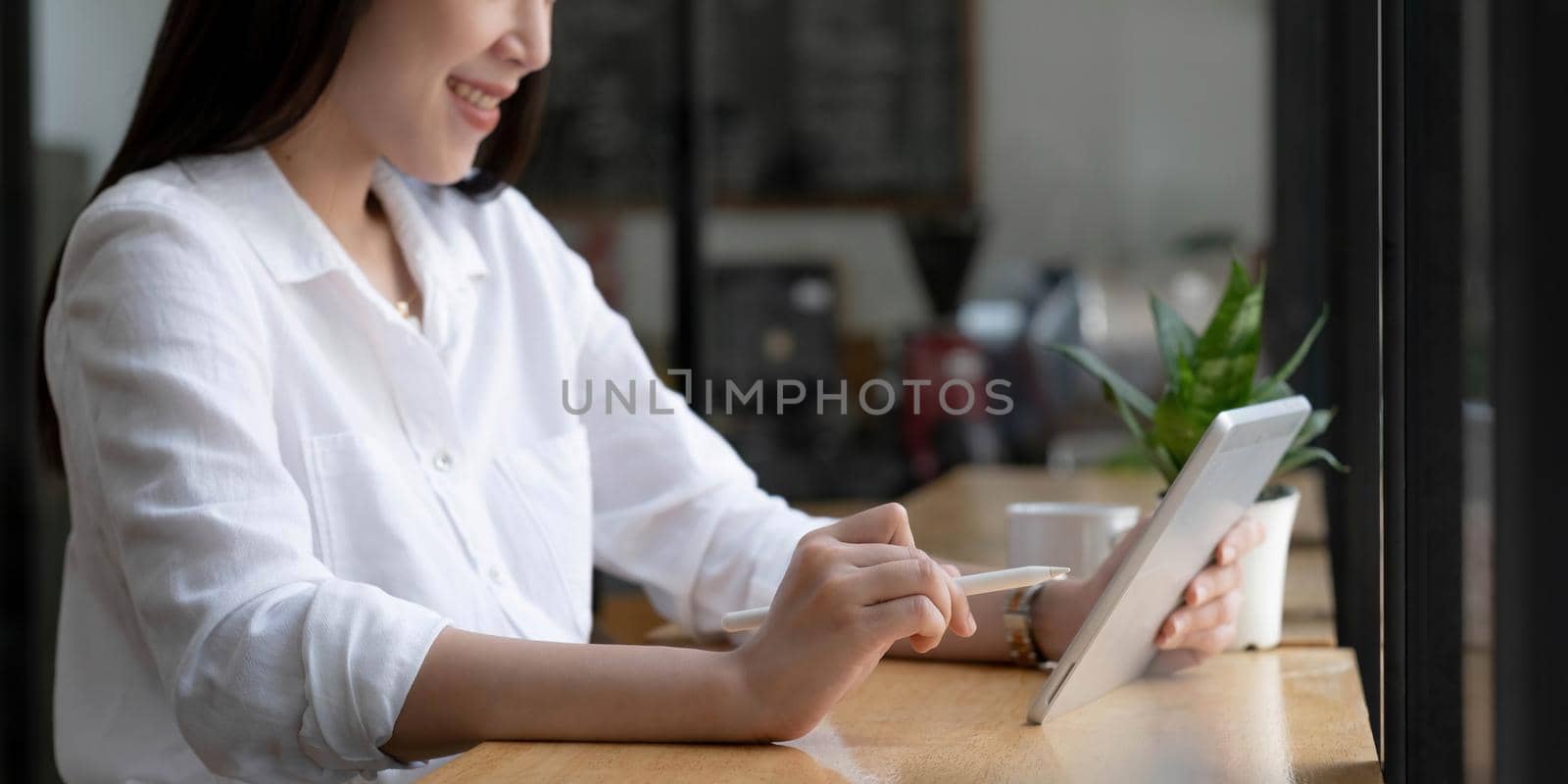 Beautiful young Asian woman or female college student relaxes sitting in the coffee shop and using portable tablet touchpad. by wichayada