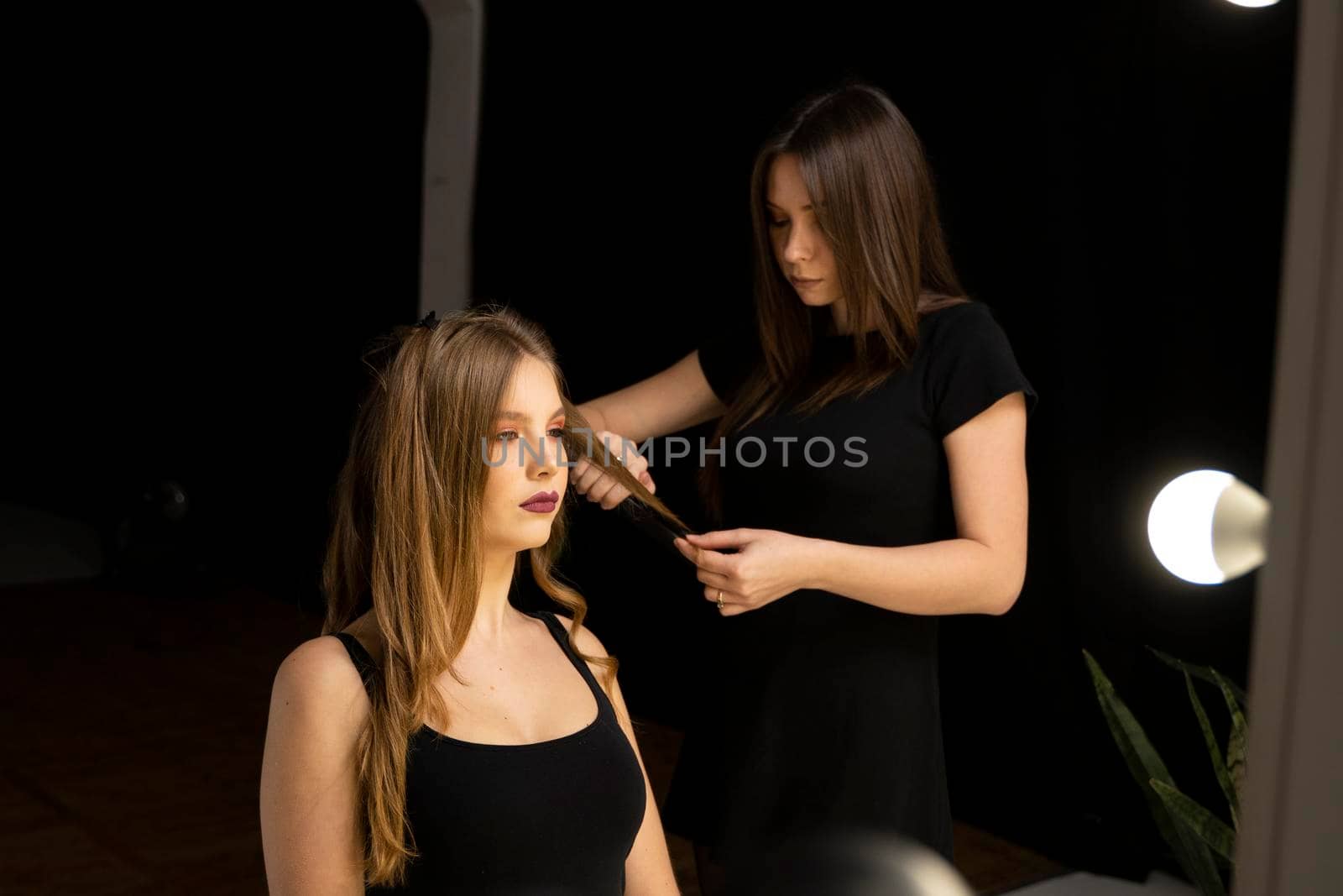 Professional hair care and creating hairstyles. Bride with brown curly long hair in a beauty salon is preparing for the wedding day