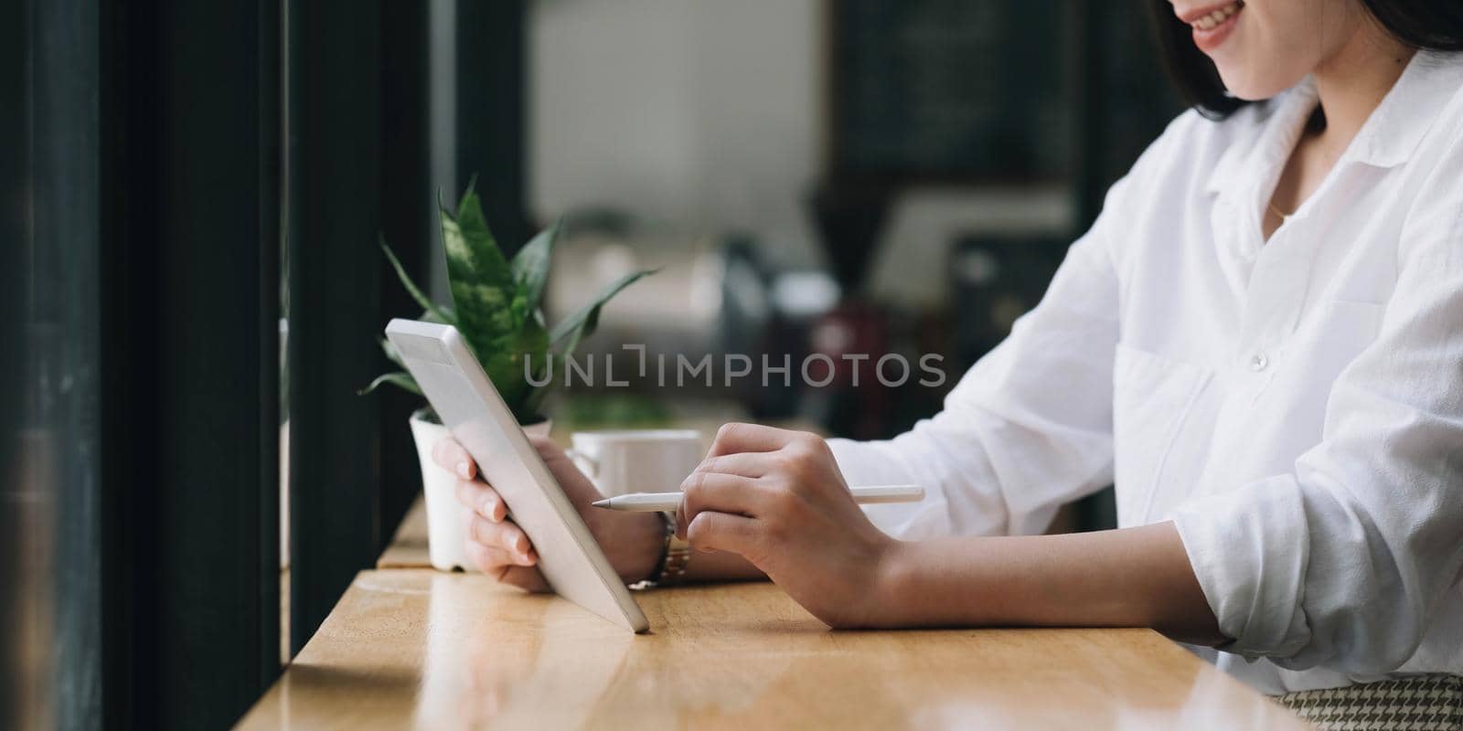 Beautiful young Asian woman or female college student relaxes sitting in the coffee shop and using portable tablet touchpad..