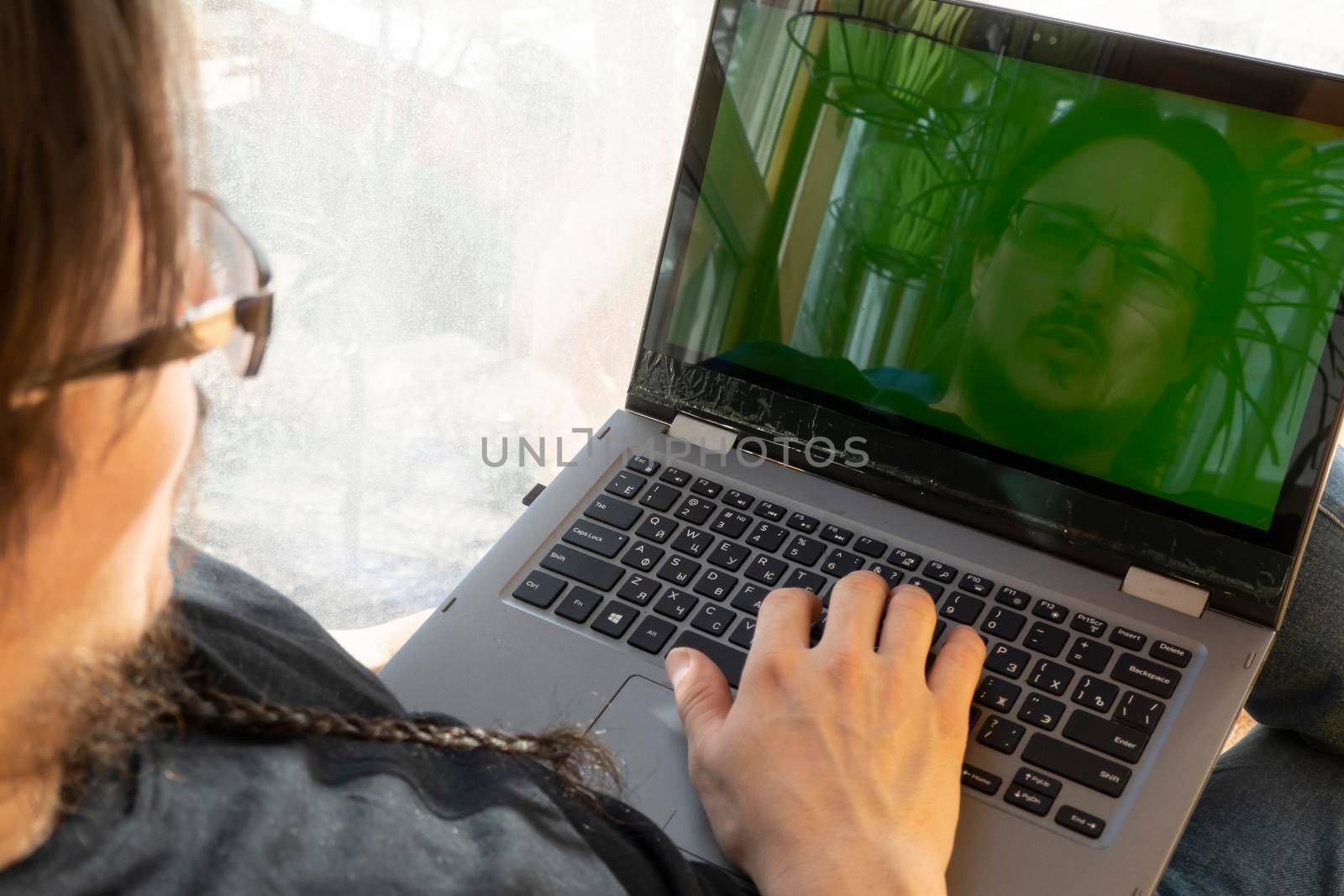 serious man sits in a blue bean bag chair and uses a laptop indoors. home office on the balcony. freelancing and remote work concept