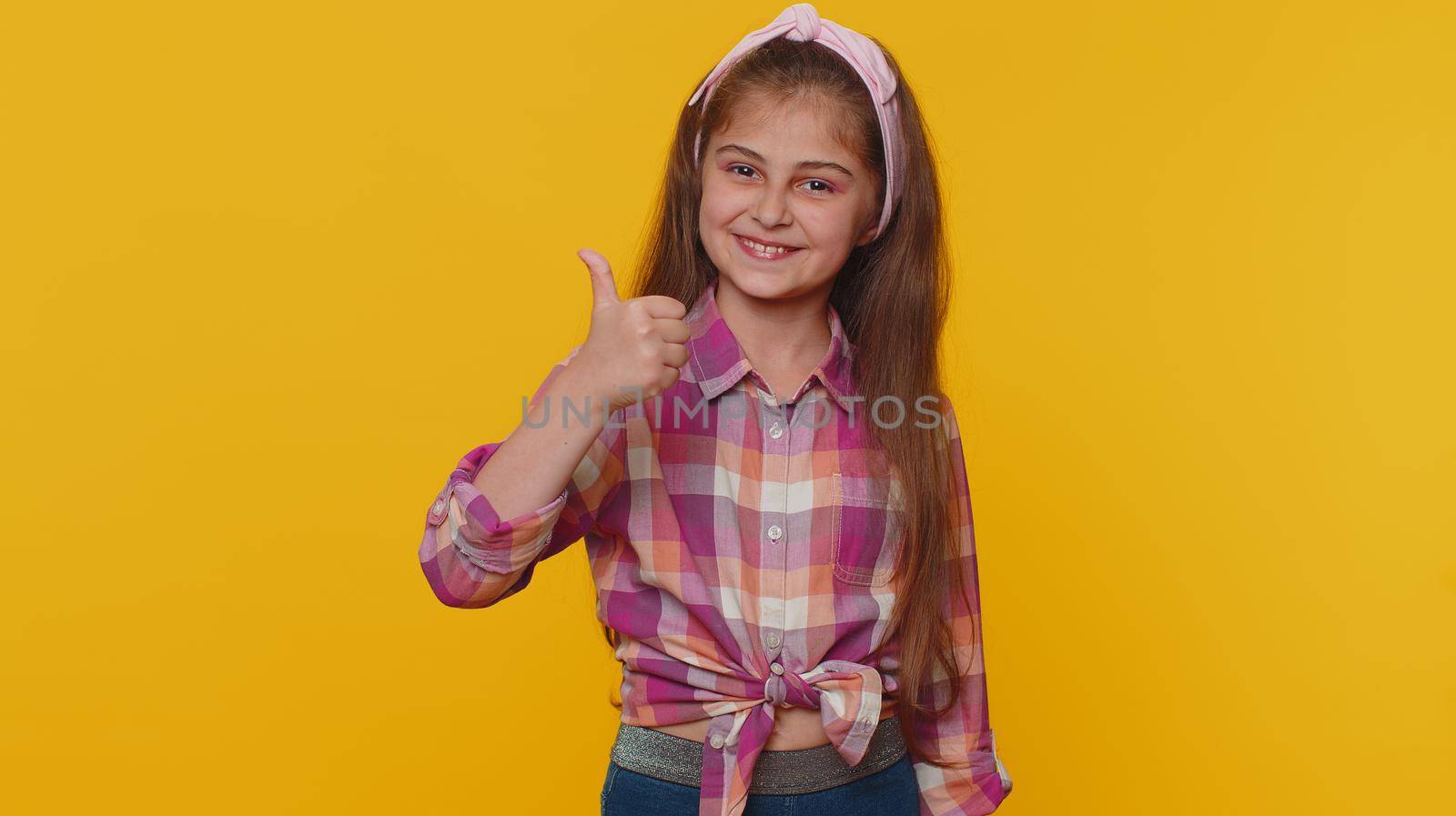 Like. Happy young preteen child girl kid looking approvingly at camera showing thumbs up, like sign positive something good, positive feedback. Toddler children isolated on studio yellow background