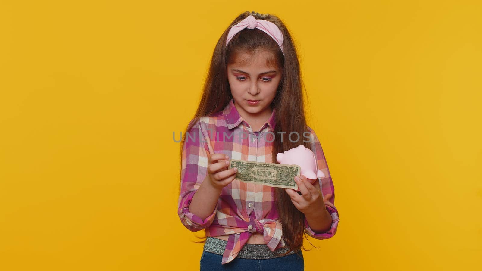 Poor young preteen child girl kid insufficient amount of money, holding piggybank and one dollar banknote at home. Financial crisis. Bankruptcy. Poverty and destitution. Little toddler children alone