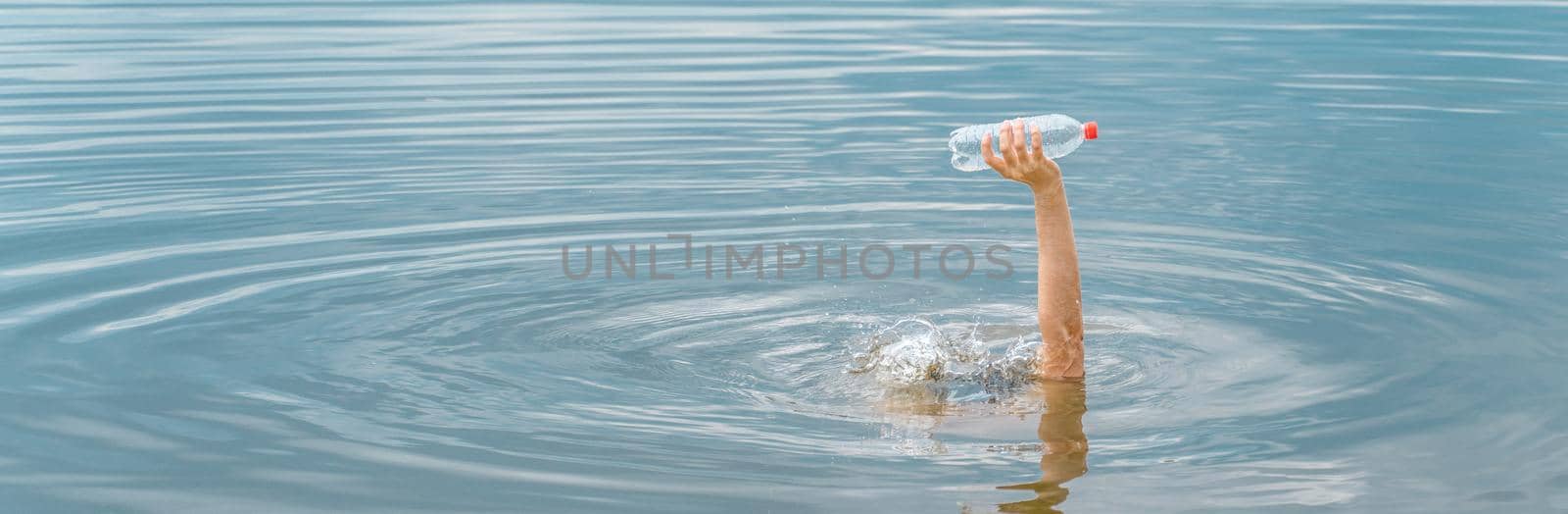 Raised hand holding bottle plastic garbage beach pollution water environment and plastic concept. Save ocean plastic pollution. Cleaning trash water. Empty bottle hand success nature pollution concept by synel