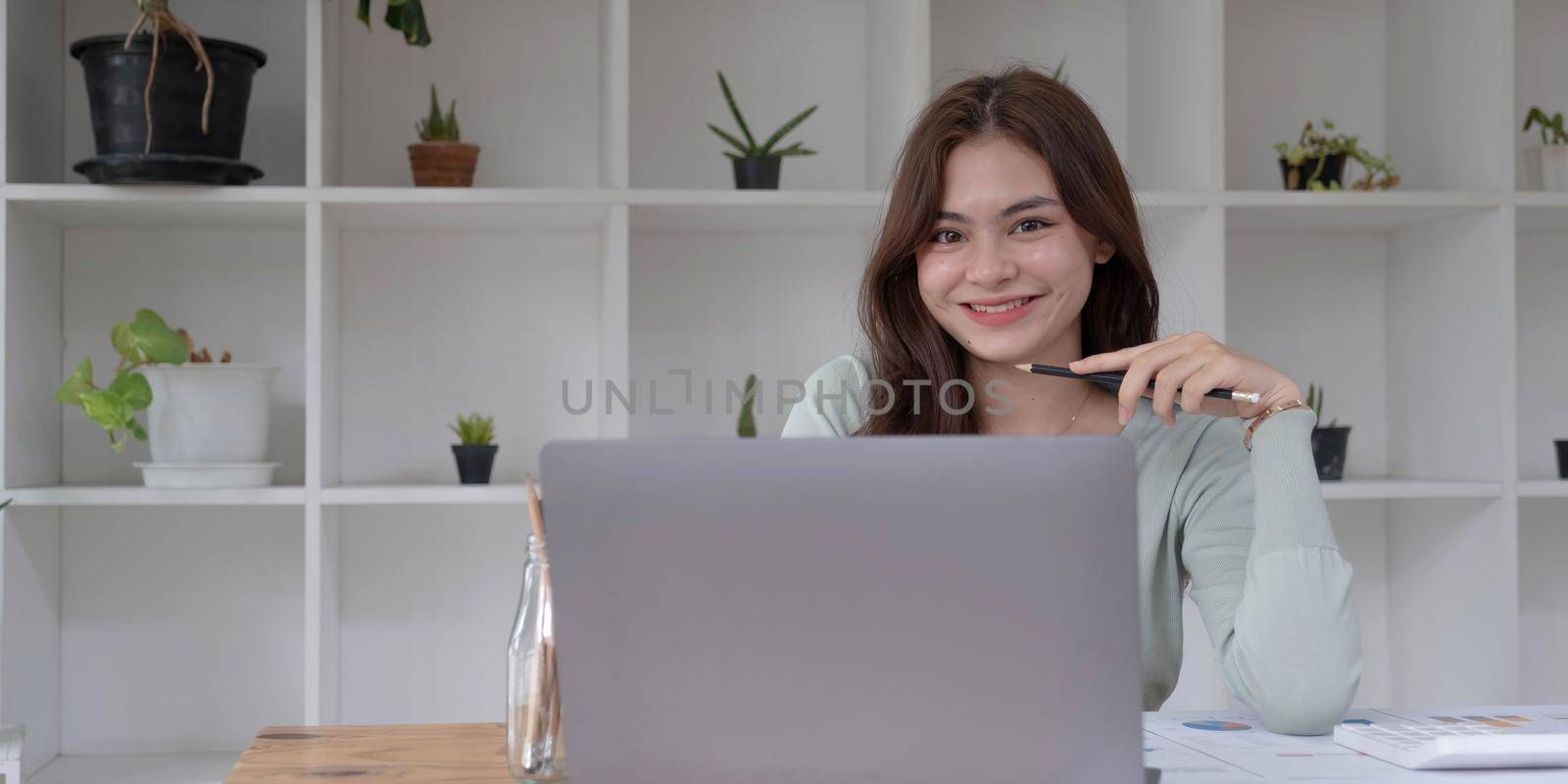 Charming Asian woman working at the office using a laptop Looking at the camera. by wichayada