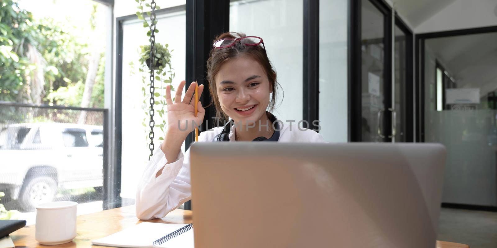 Happy young asian teen girl sit on sofa at home holding phone looking at screen waving hand video calling distance friend online in mobile chat app using smartphone videochat application..