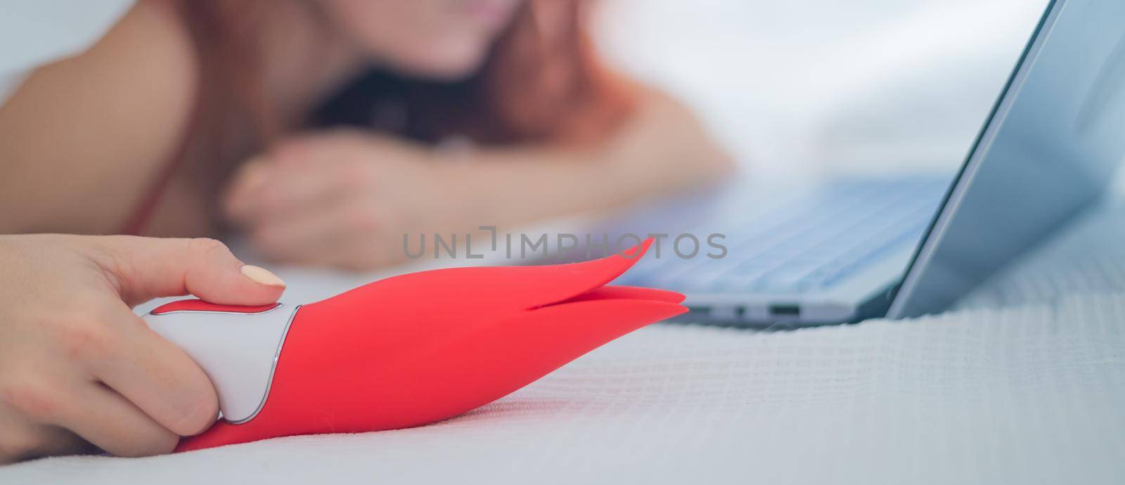 A woman lies in bed holding a clitoral vibrator and watching porn on a laptop. The girl has sex online by mrwed54