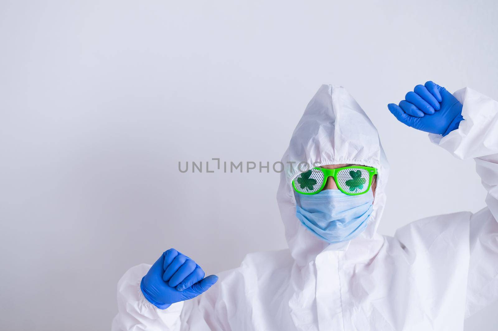 A woman in a protective suit and a medical mask and wearing funny glasses celebrates st patrick's day.