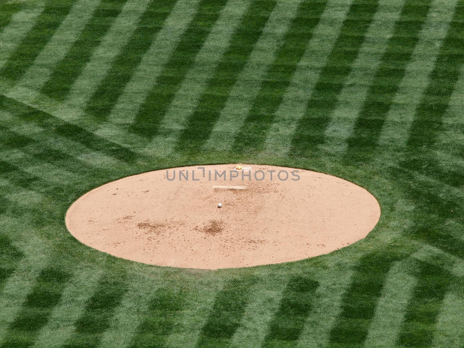 Baseball mound sits empty in with baseball and rosin bag during game.