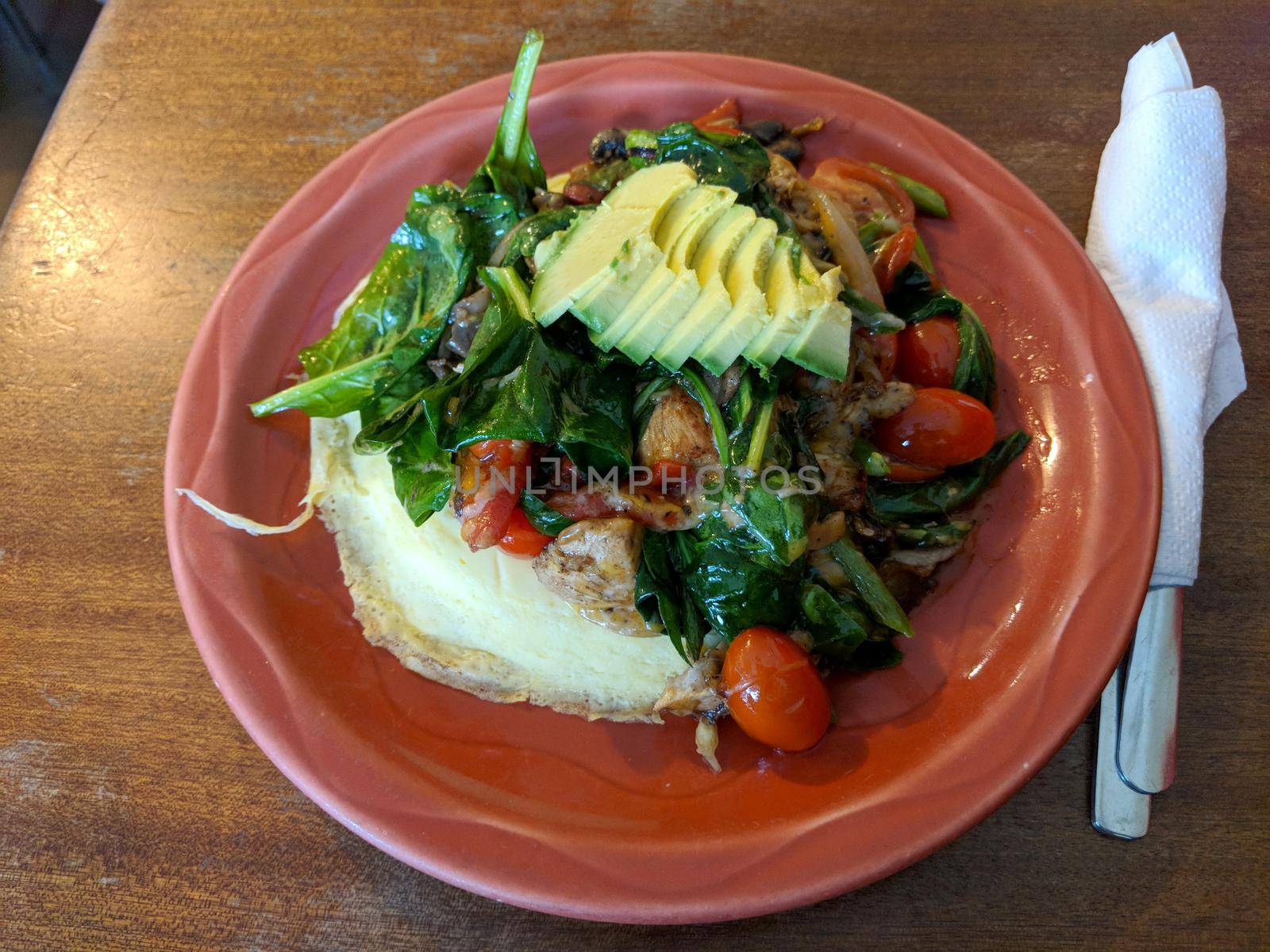 Omelette with Avocado, tomatoes, spinach, and asparagus on top of it on red plate and table.