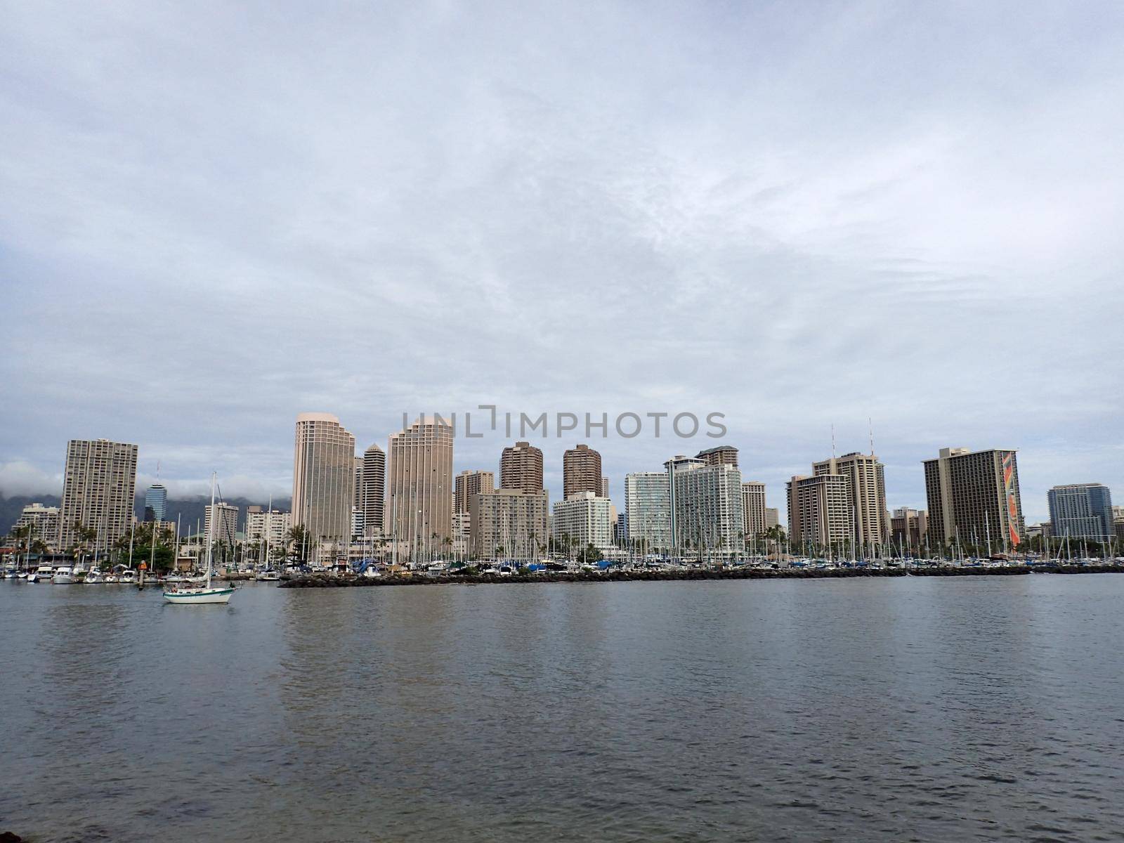Honolulu - February 23, 2018:  Boat sails by Ala Wai Boat Harbor, and Waikiki Hotels during a beautiful day with clouds on the island of Oahu, Hawaii.