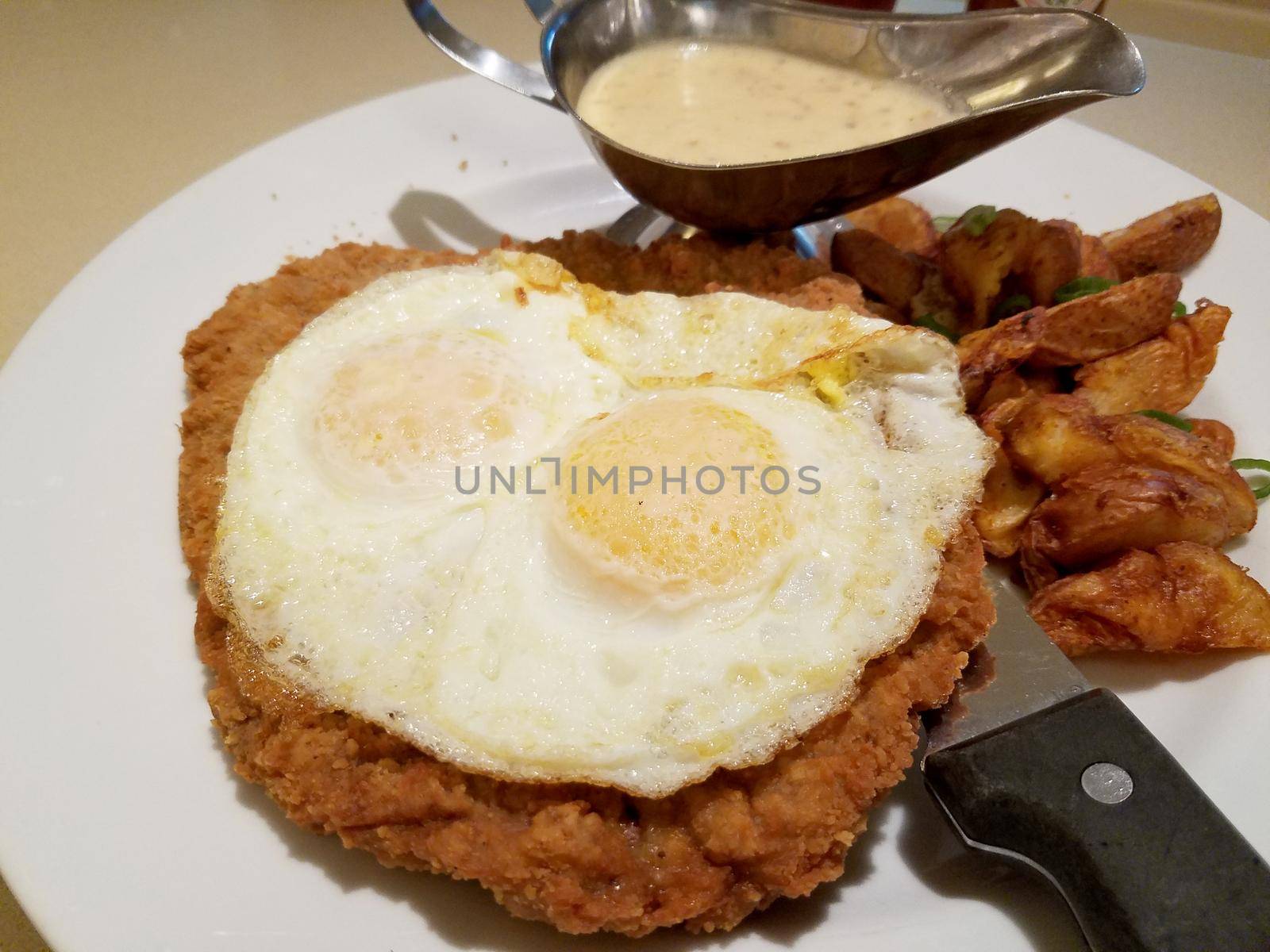 Chicken Fried Steak - two eggs over easy, country gravy, breakfast potatoes on plate with steak knife.