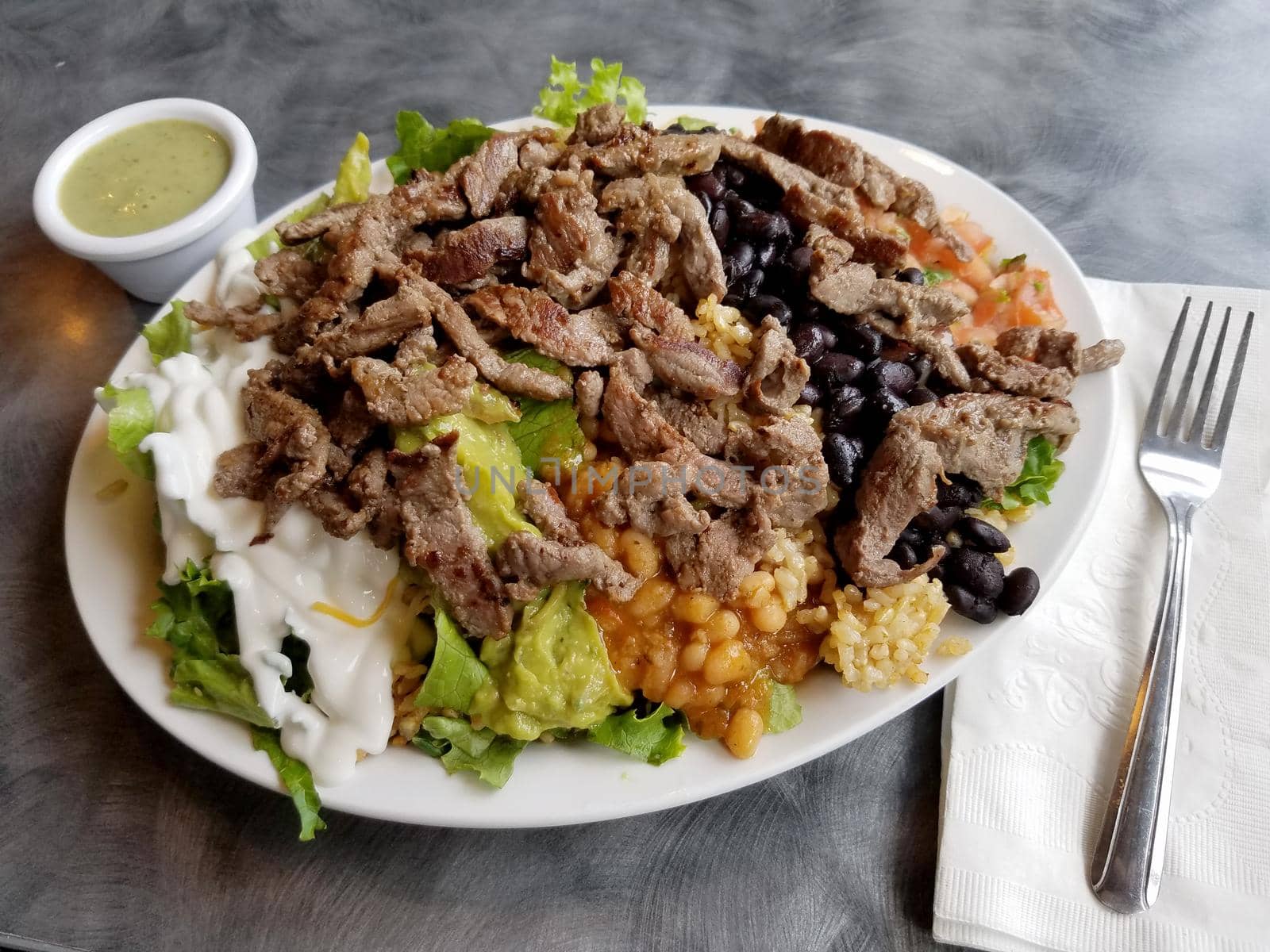 Outer Reef Salad featuring Steak, Rice, Black beans, Cajun White Beans, Red Cabbage, Cheese, Salsa, Guacamole, Sour Cream, and salad dressing.
