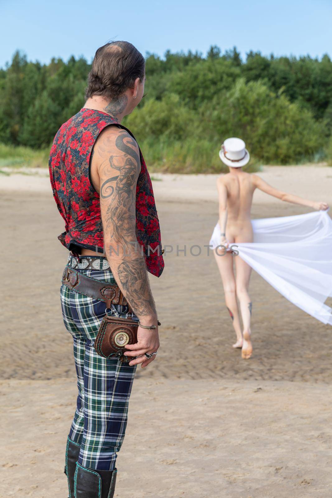 AINAZI, LATVIA – Jul 29, 2019: Love story. Non-traditional wedding photo shoot on the shores of the Baltic Sea. Nude bride in a veil and a spectacular groom