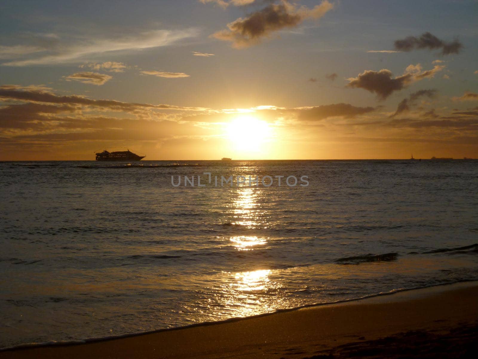 Super Sunset though the clouds and reflecting on the Pacific ocean on the water with boats off the coast of Oahu, Hawaii.