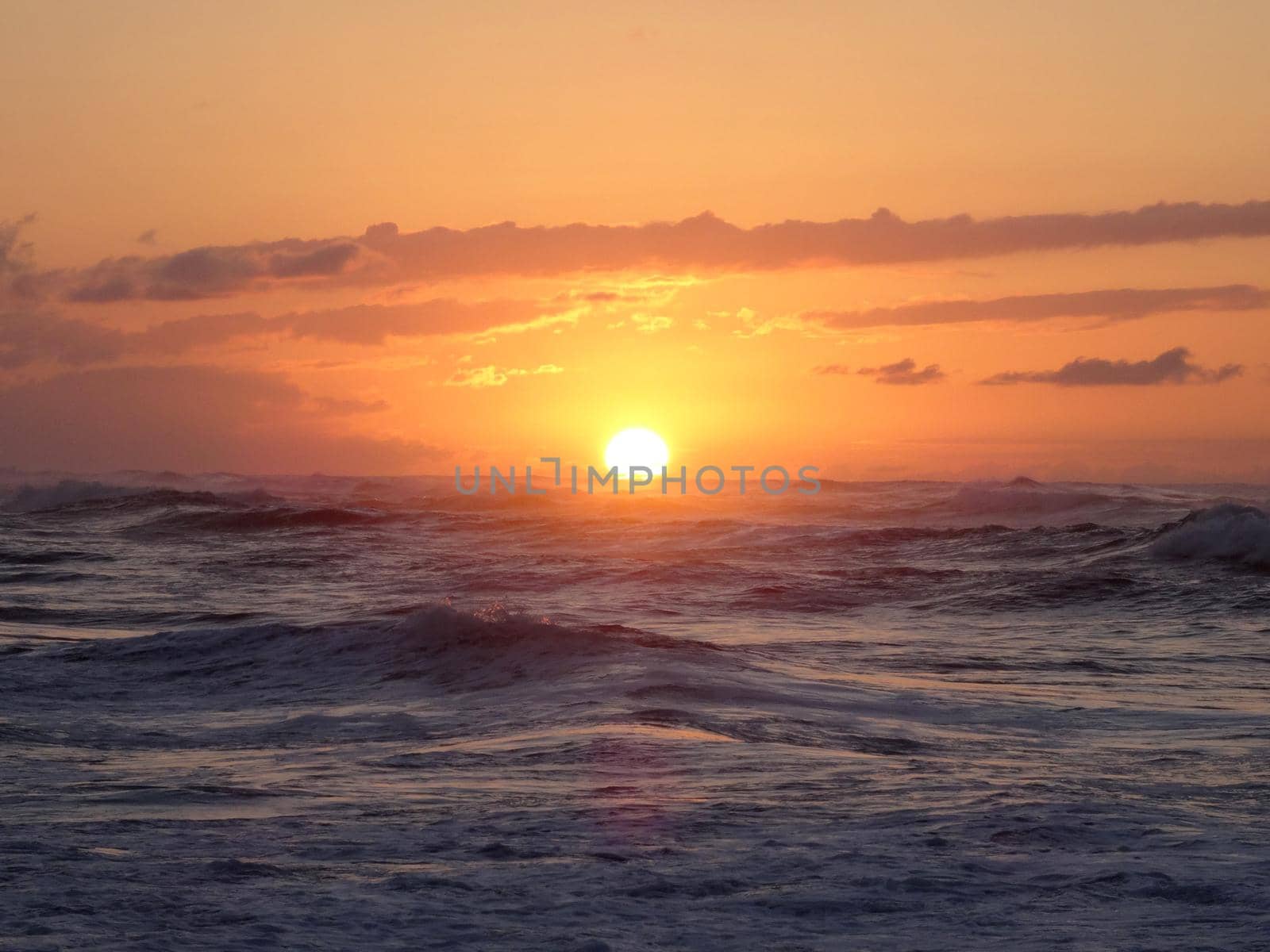 Sunset into the ocean with waves rolling towards shore on the North Shore of Oahu.    