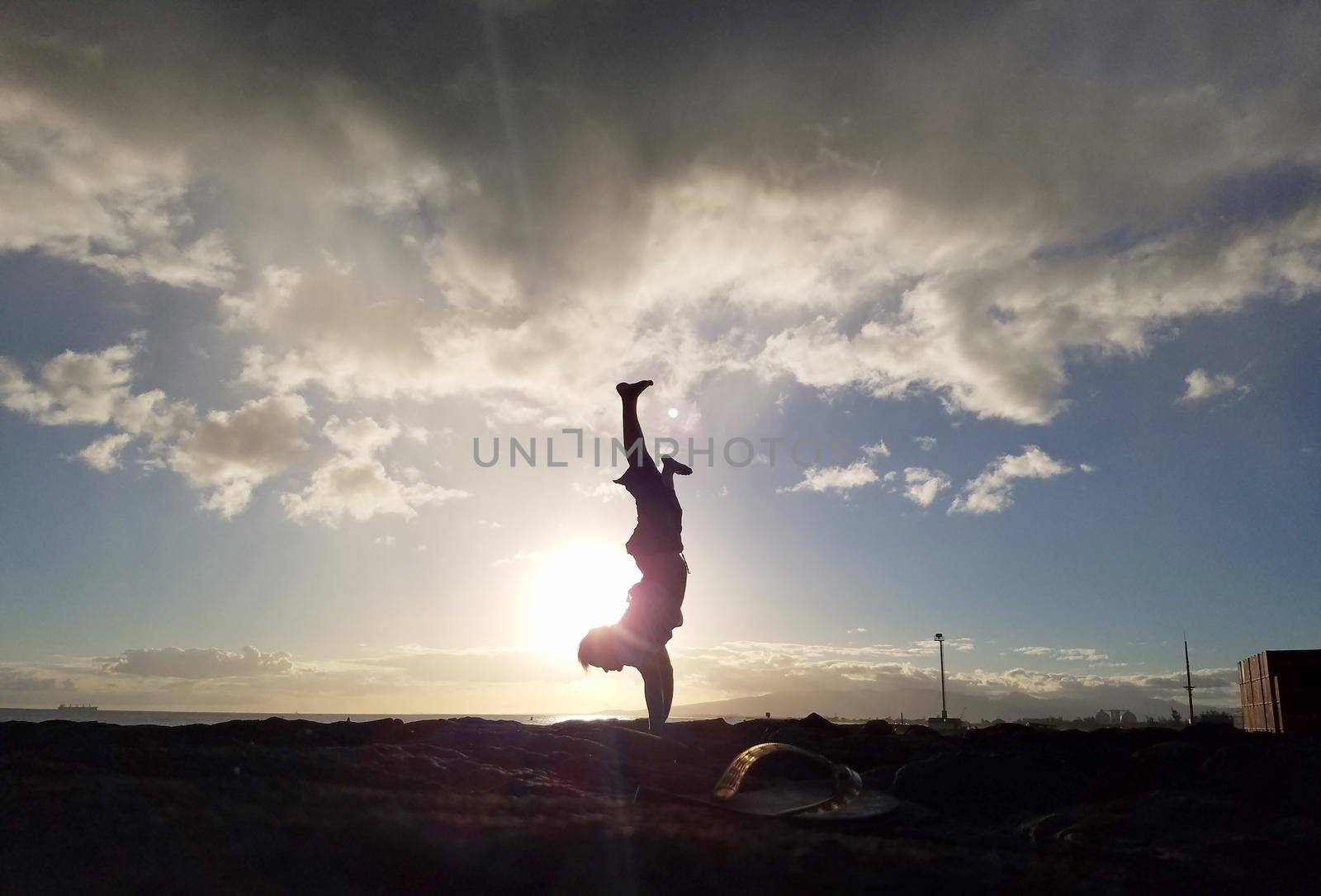 Man split leg Handstand on coastal rocks at sunset with boats on ocean on Oahu, Hawaii.                    