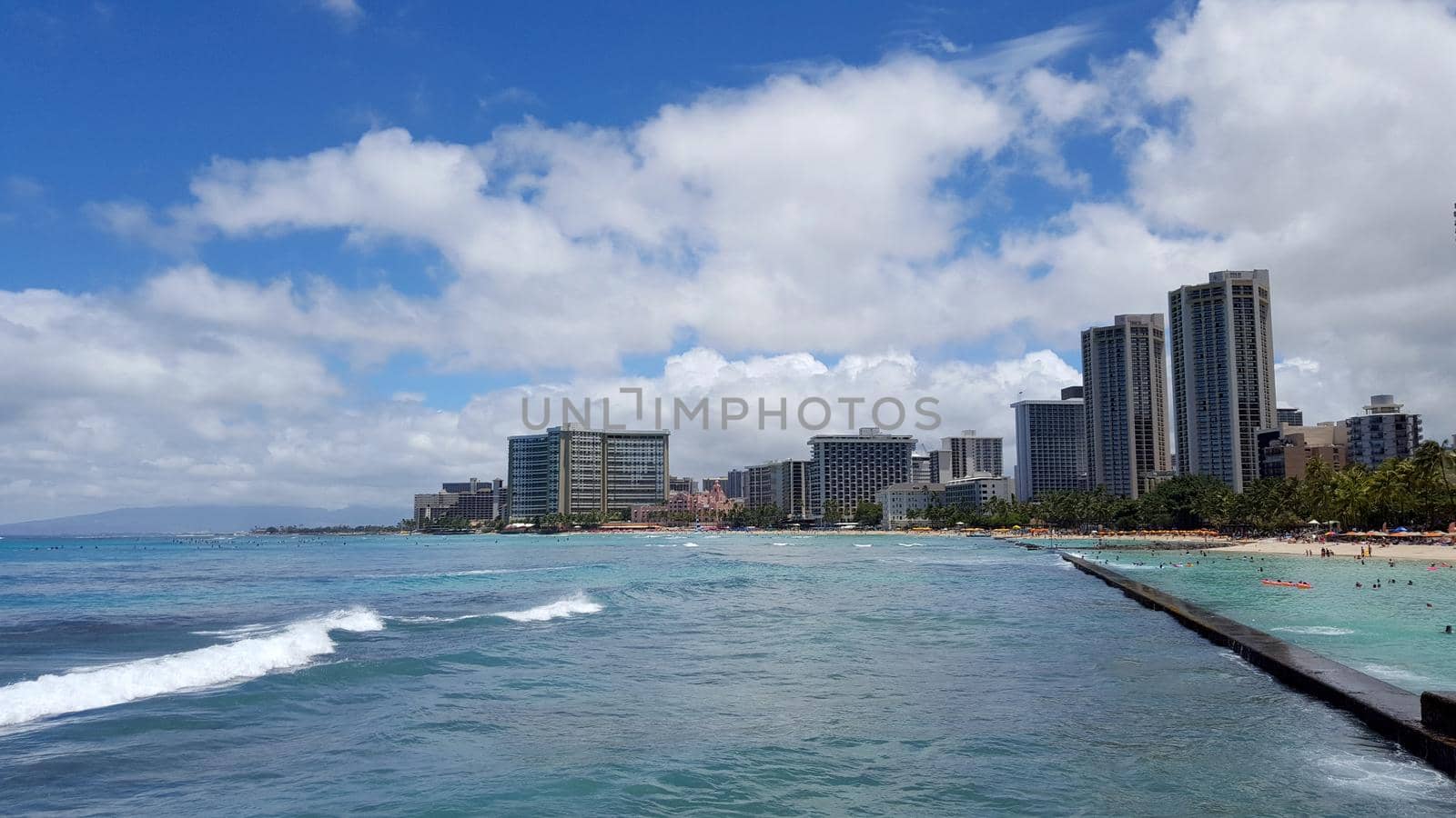 Waikiki - July 3, 2016: Waves roll into shore as People play in the protected water and hang out on the beach in world famous tourist area Waikiki on a beautiful day with hotels in the distance.  June 17 2014 in Waikiki, Hawaii.