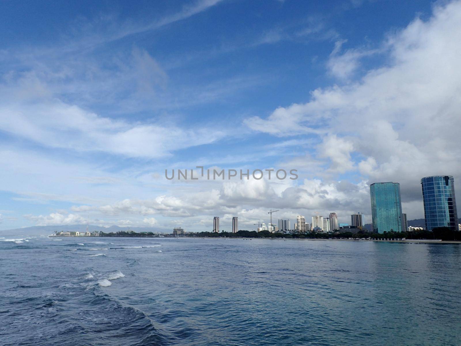 waves in the water of Ala Moana Beach with Condo buildings and construction cranes in the distance during a beautiful day on the island of Oahu, Hawaii. 