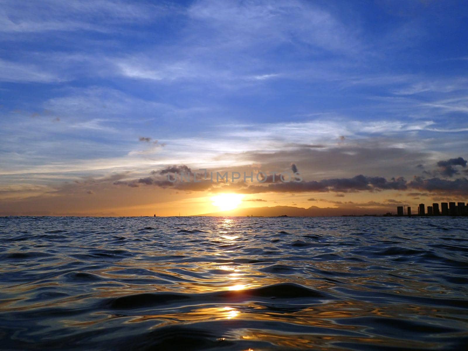 Sunsets over Waianae mountains with light reflecting on ocean and illuminating the sky with boats sailing on the water off Waikiki on Oahu, Hawaii.