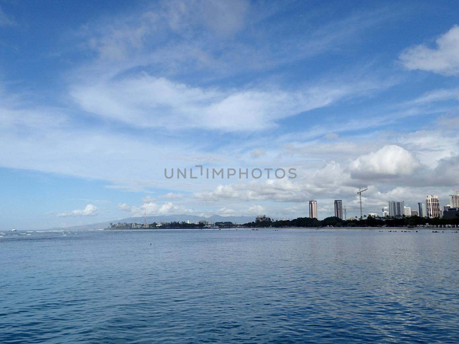 Glassy water of Ala Moana Beach with Condo buildings and construction cranes in the distance during a beautiful day on the island of Oahu, Hawaii. 