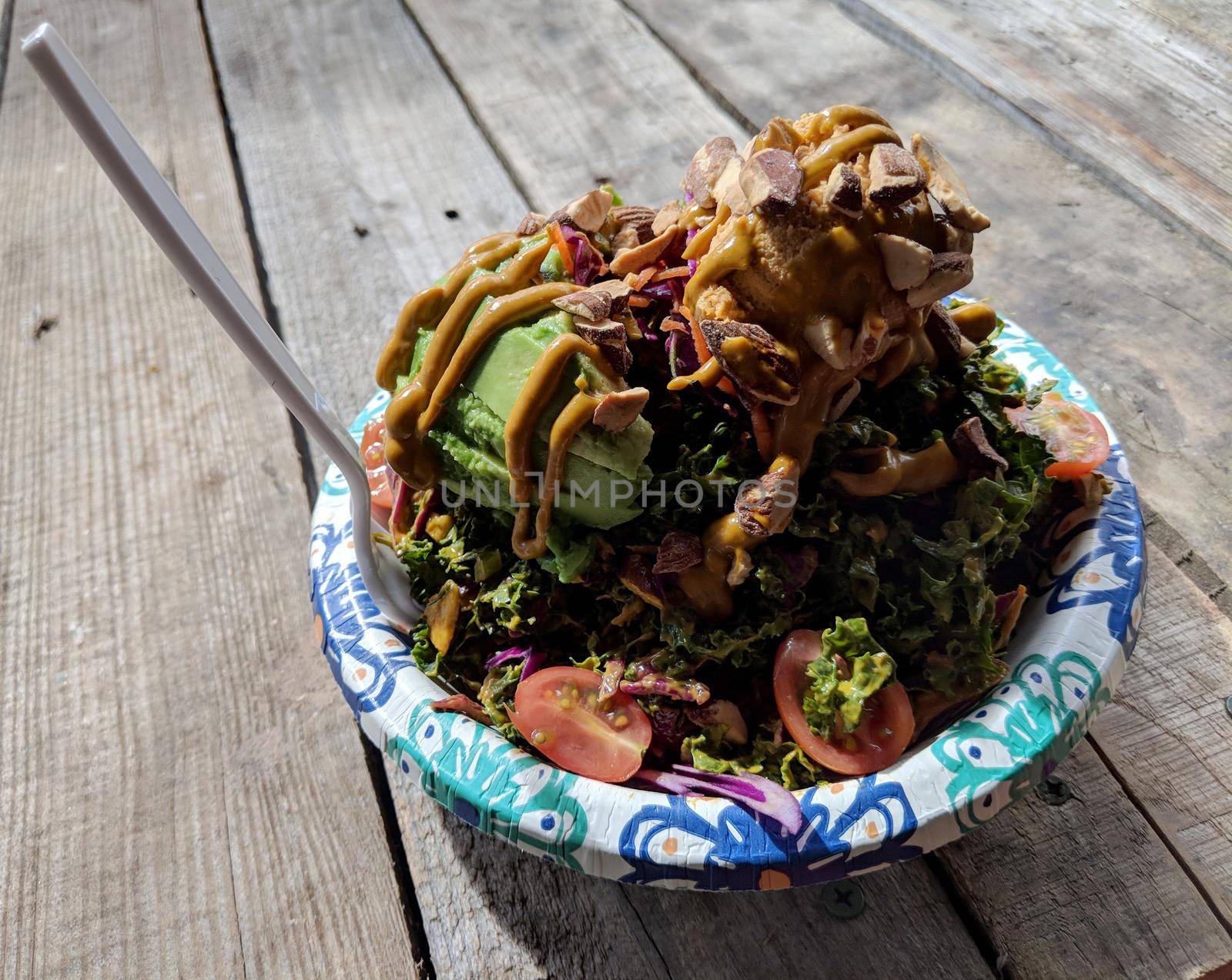 Rainbow Bowl: Kale salad with red cabbage, green onion, carrot, Japanese  cucumbers tossed in ginger tahini dressing.  Served on brown rice.  Topped with avocado, grape tomato, veggie mix, almonds and hummus. 