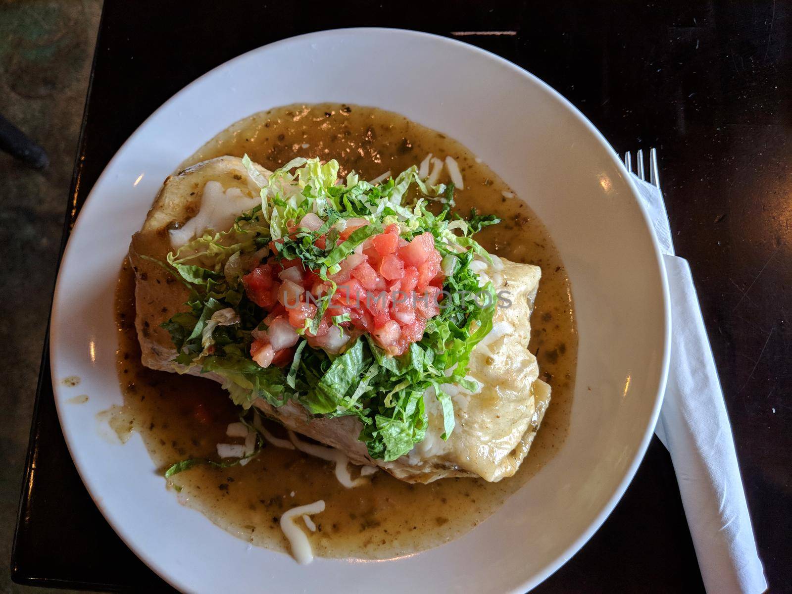 Ultimate Cali Burrito smothered 'wte-style' with green chile sauce, cheese, tettuce and pico de gallo on a white plate.