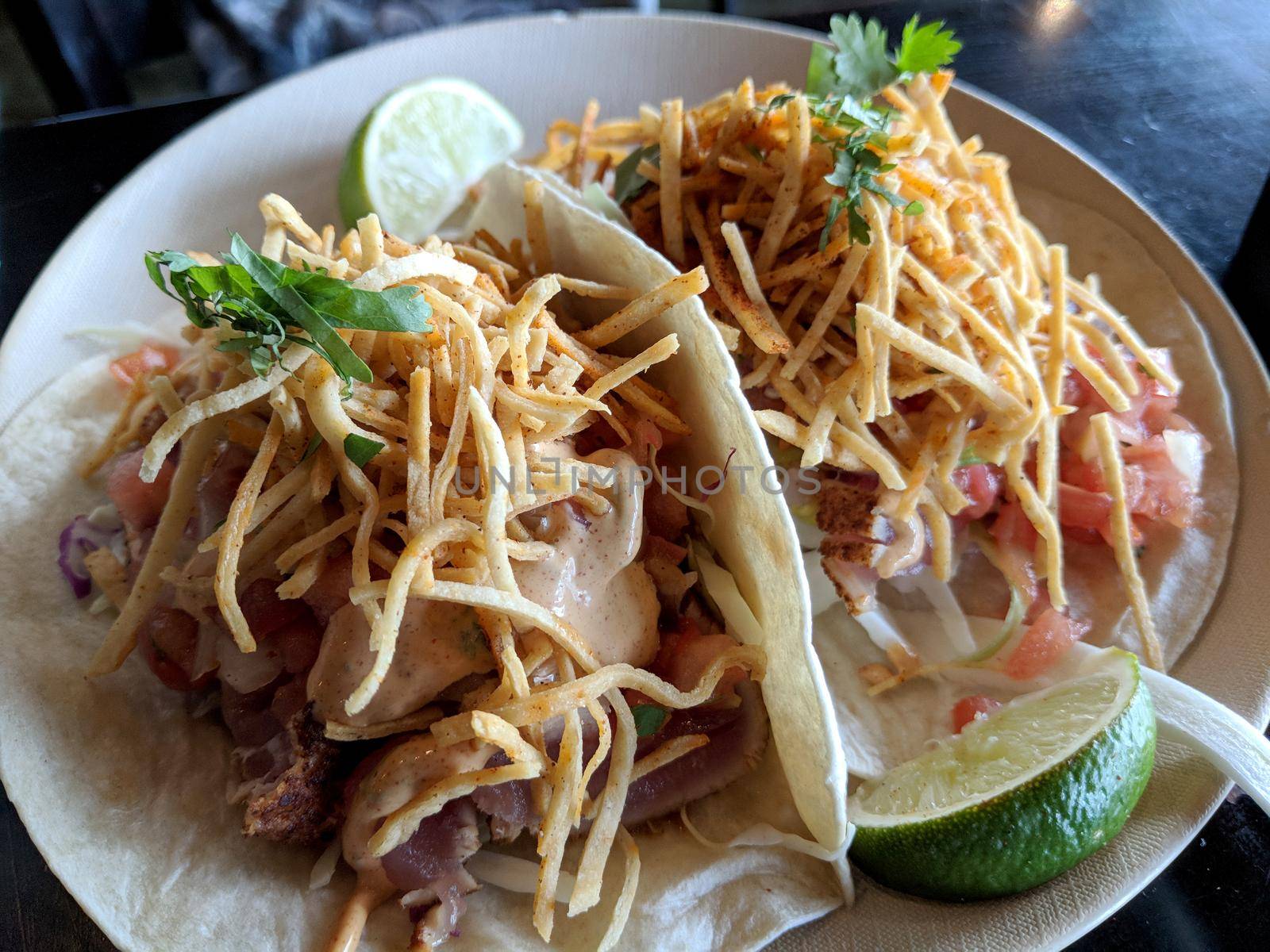 Fish Tacos - Flour tortillas, cabbage, guacamole, corn strips, pico de gallo, signature aioli locally caught seared rare ahi on white plate.