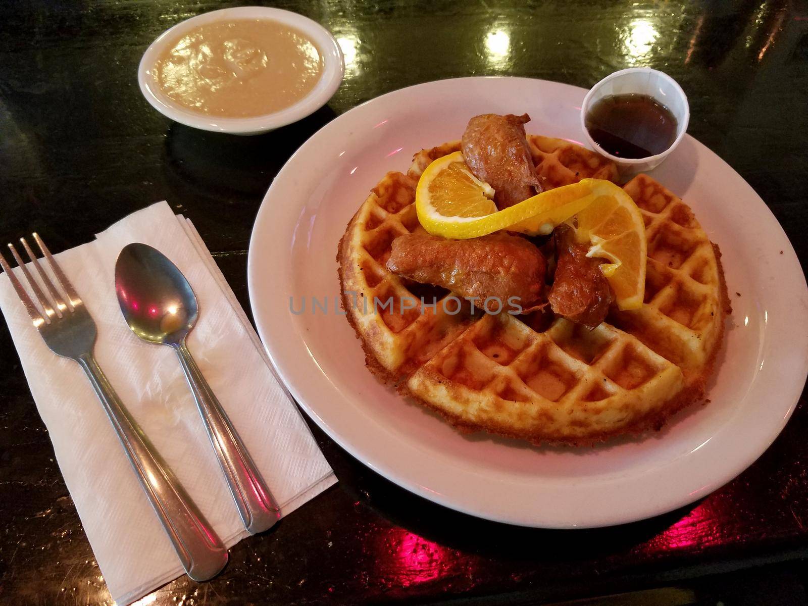 Vegetarian Chicken and waffles on a white plate with Gravy on the side and orange slice.  Chicken and waffles is an American dish combining chicken with waffles. It is part of a variety of culinary traditions, including soul food and Pennsylvania Dutch cuisine, and is served in certain specialty restaurants in the United States.