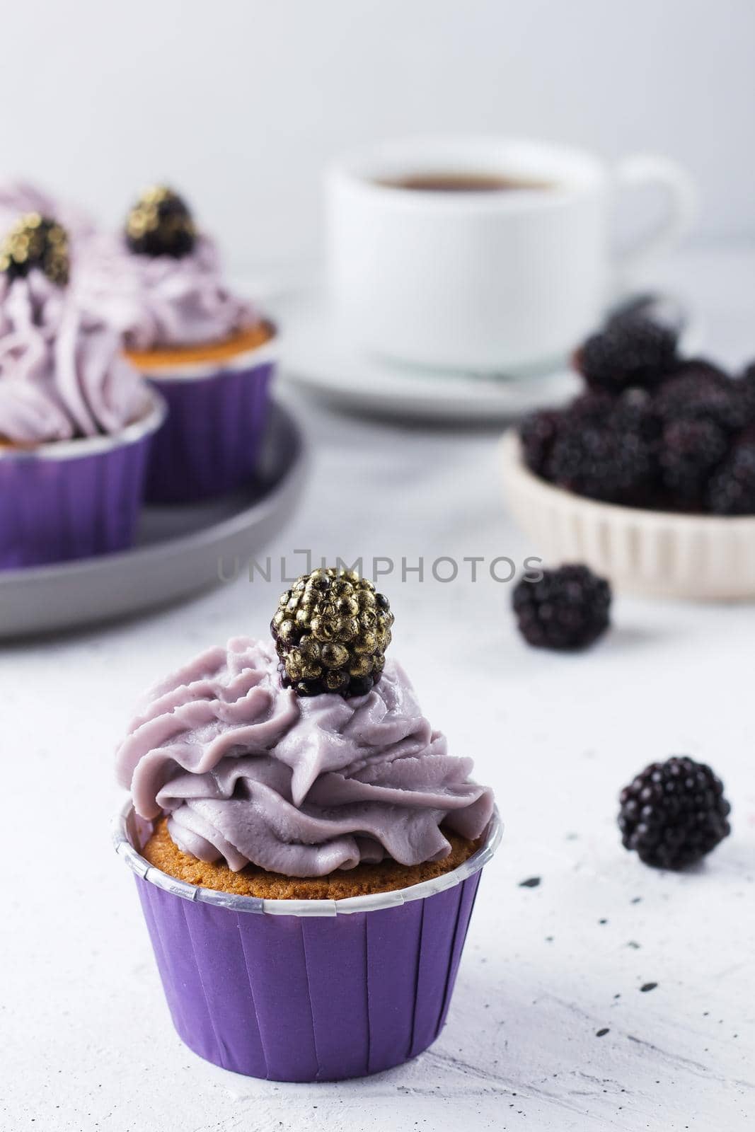 Delicious blackberry cupcake on a gray background with berries, tea and cupcakes in the background. Vertical photo