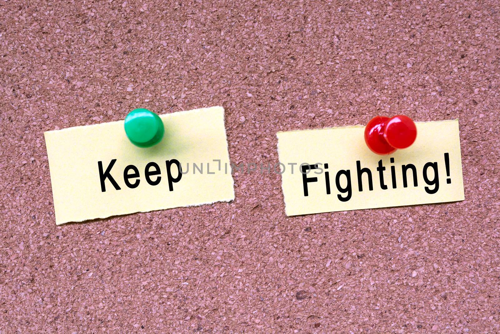 Keep fighting words on stick note and blue pinned to a cork notice board. Business concept.