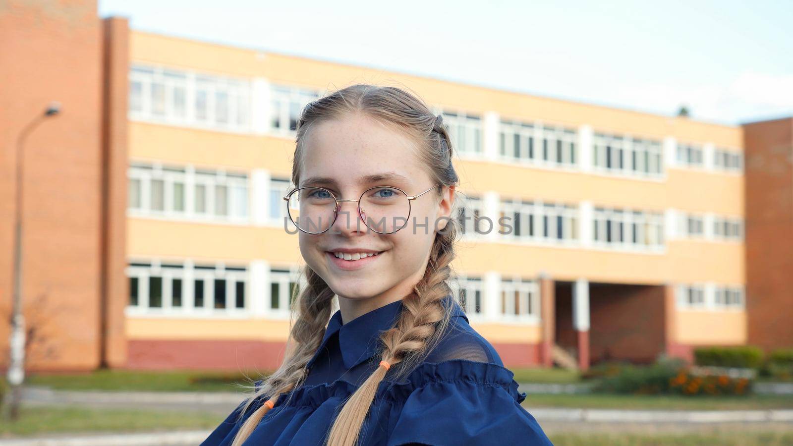 A teenage girl wearing glasses in front of a school