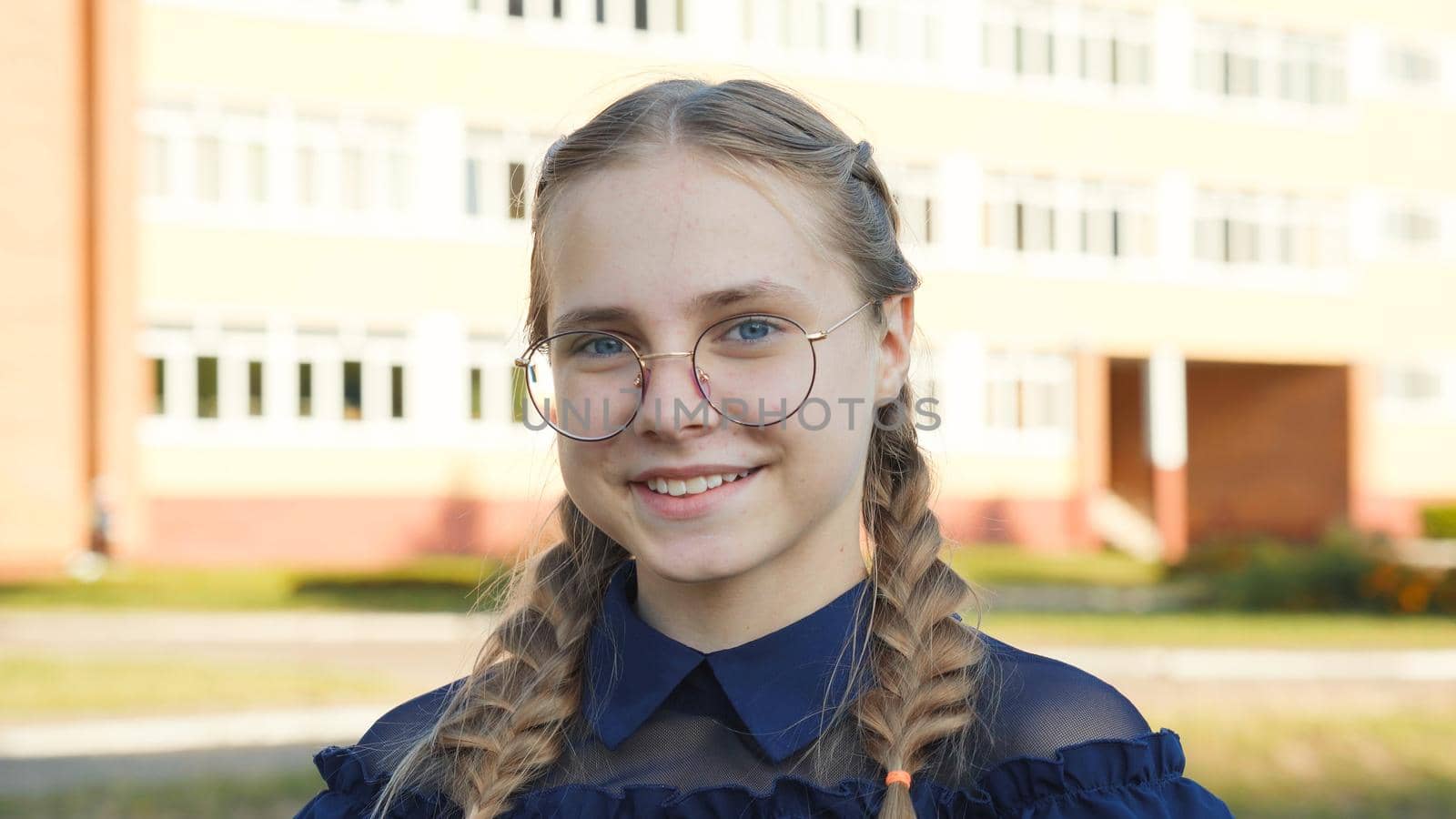 A teenage girl wearing glasses in front of a school