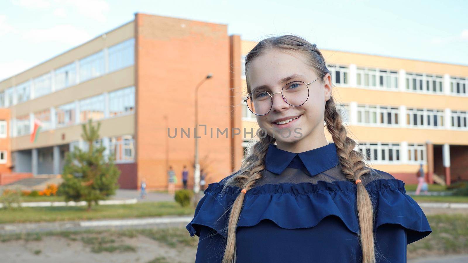 A teenage girl wearing glasses in front of a school