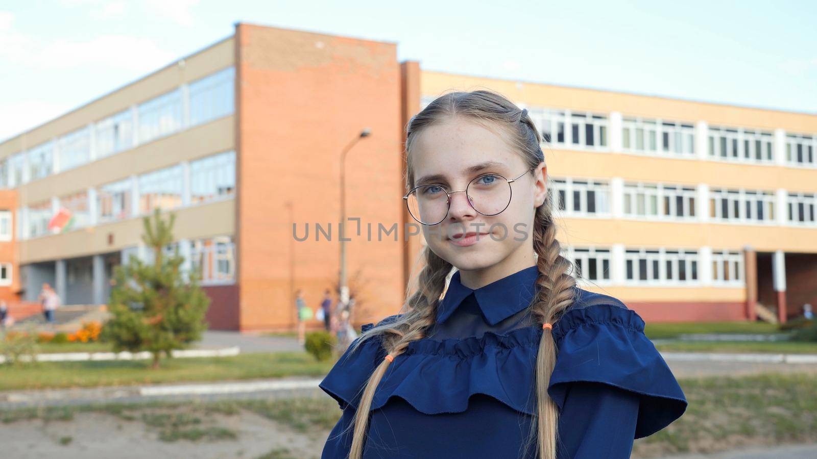 A teenage girl wearing glasses in front of a school