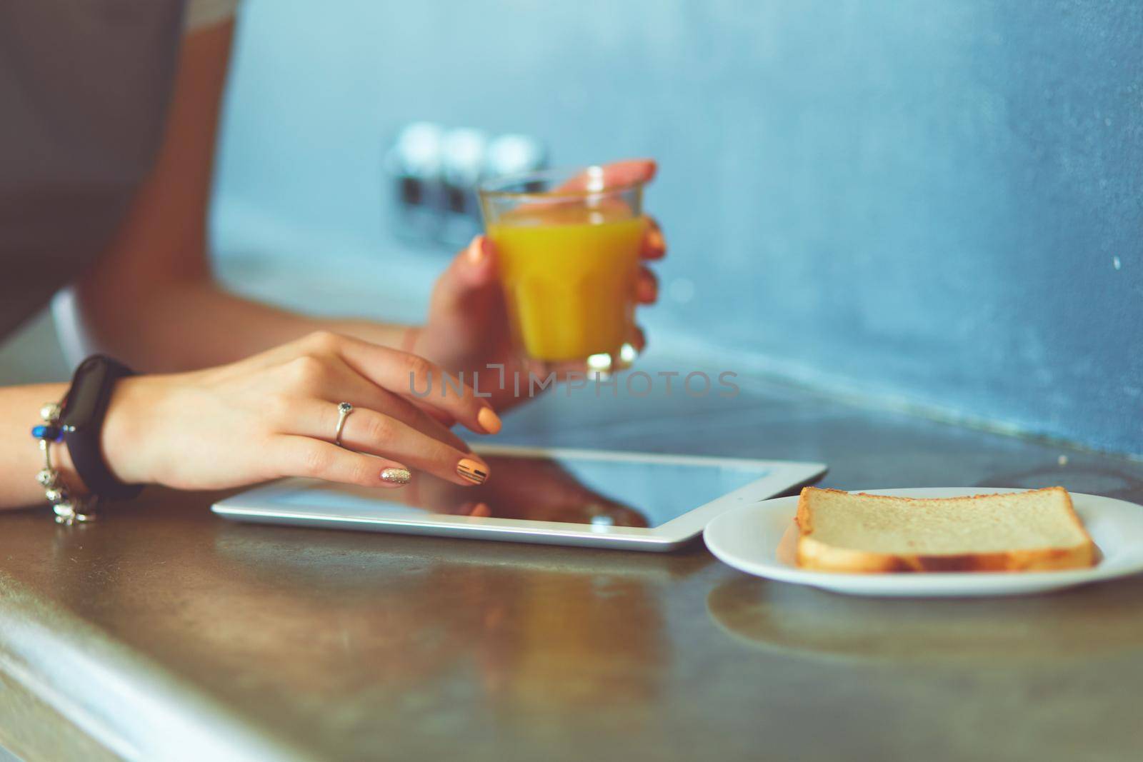 Young woman with orange juice and tablet in kitchen by lenets