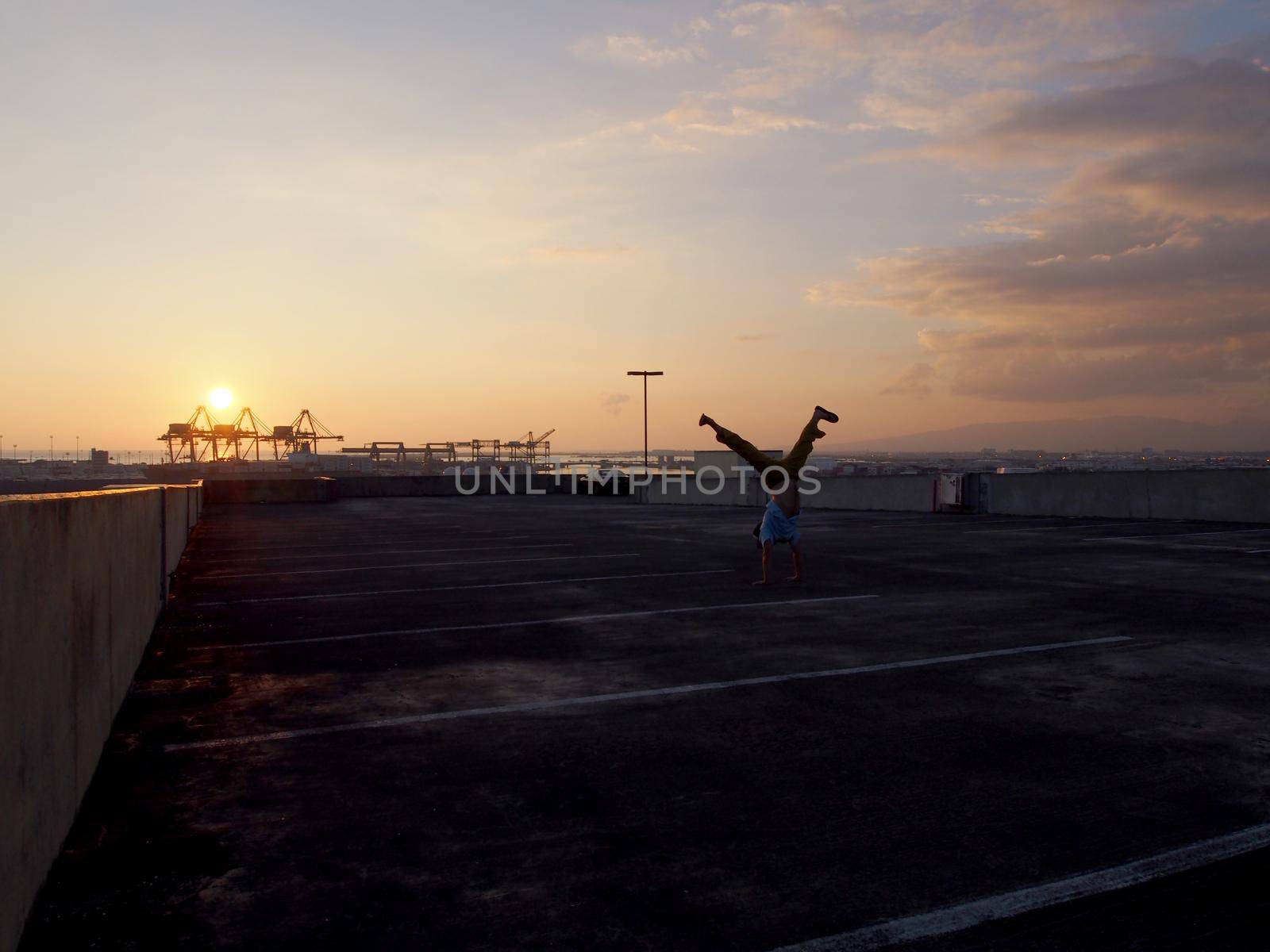 Man does Split leg Handstand on top floor of parking garage above the City of Honolulu at Sunset by EricGBVD