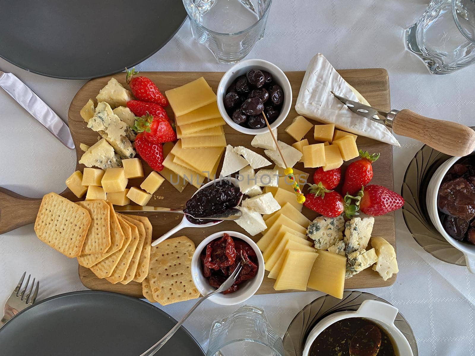Cheese plate with camembert, brie, dor blue, strawberries, sun-dried tomatoes, olives on a wooden table, top view.