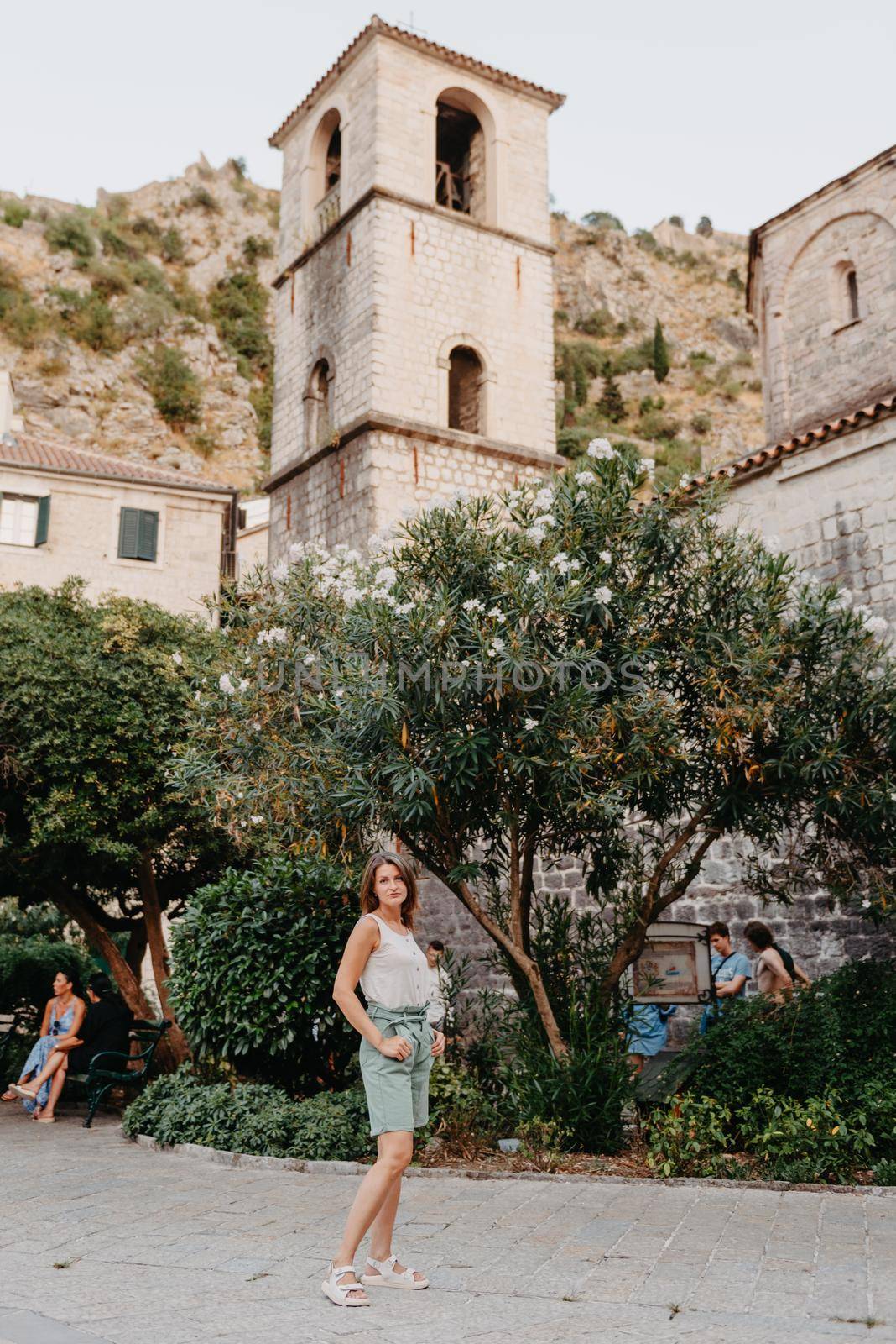 Girl Tourist Resting in the Ancient Narrow Street On A Beautiful Summer Day In MEDITERRANEAN MEDIEVAL CITY, OLD TOWN KOTOR, MONTENEGRO. Young Beautiful Cheerful Woman Walking On Old Street. Europe by Andrii_Ko