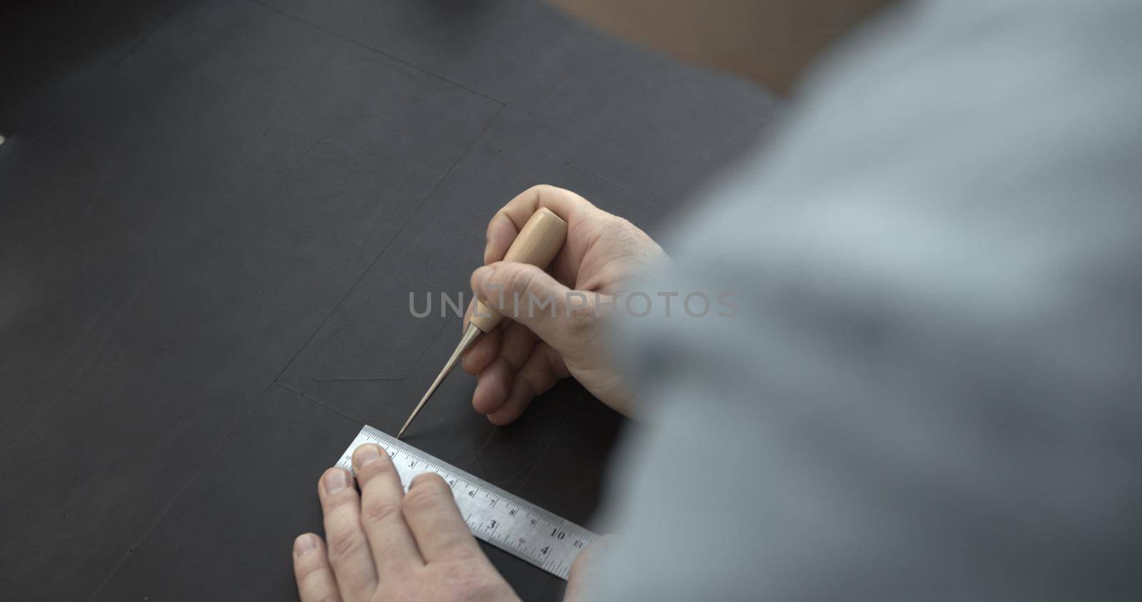 Close up of leather craftsman working with natural leather by awl and ruler. Handmade master at work in local workshop. Leather wallet stitch. by vovsht