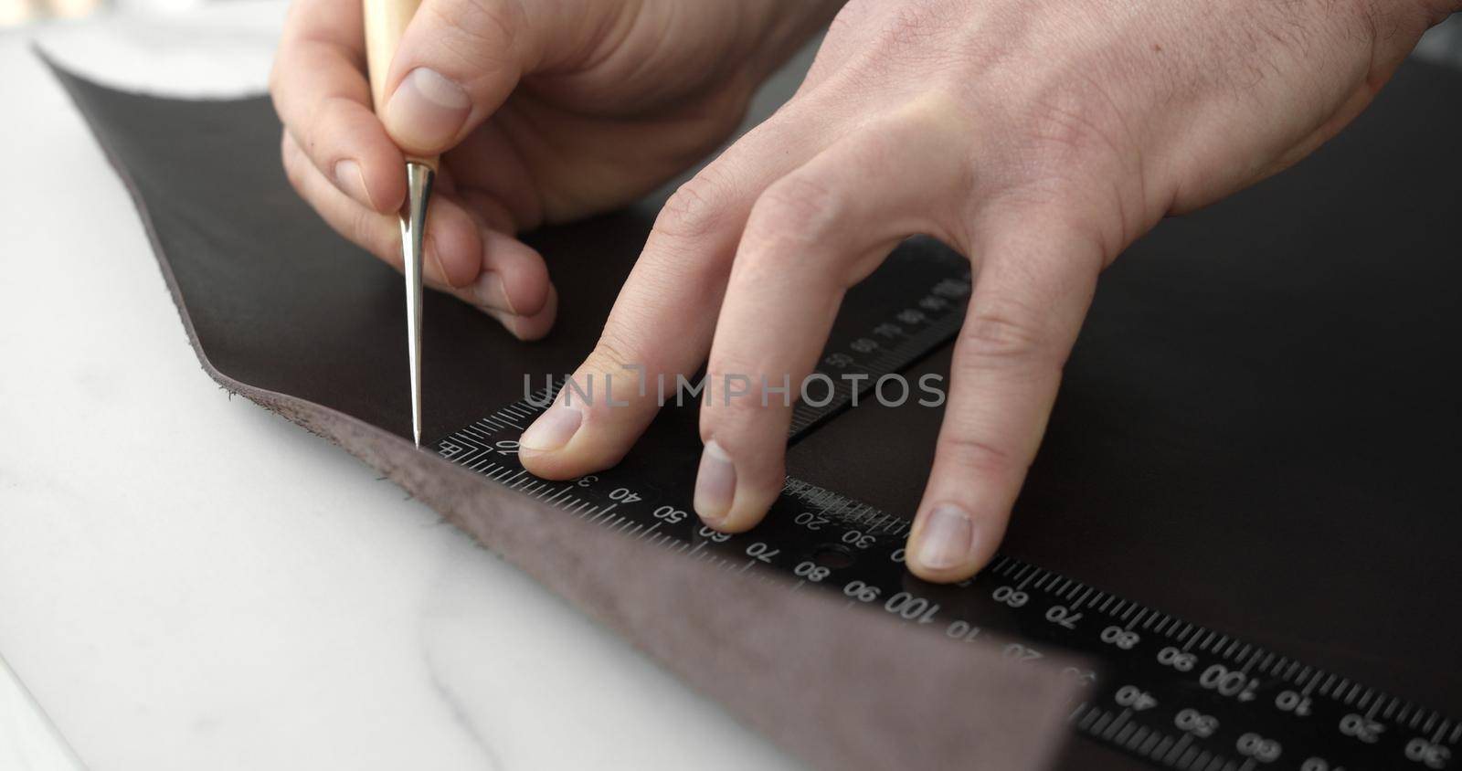 Leather craftsman working with natural leather work with awl and metal ruler adn crafting a new handmade wallet. Handmade concept. Concept of small business to create leather products