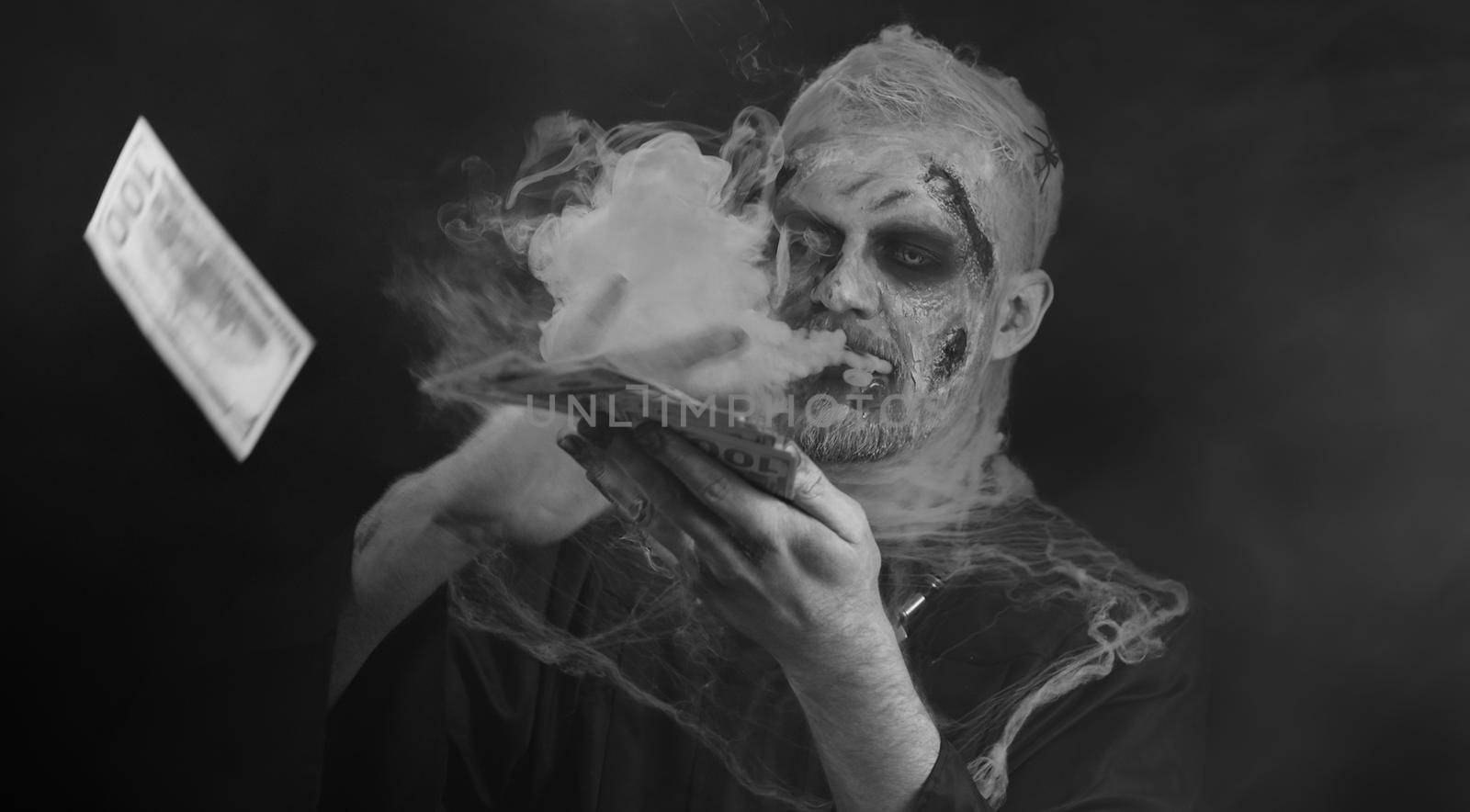 Portrait of sinister man in carnival costume of Halloween crazy zombie with bloody wounded scars face throwing money dollar cash banknotes. Horror theme of cosplay wounded undead, beast, monster