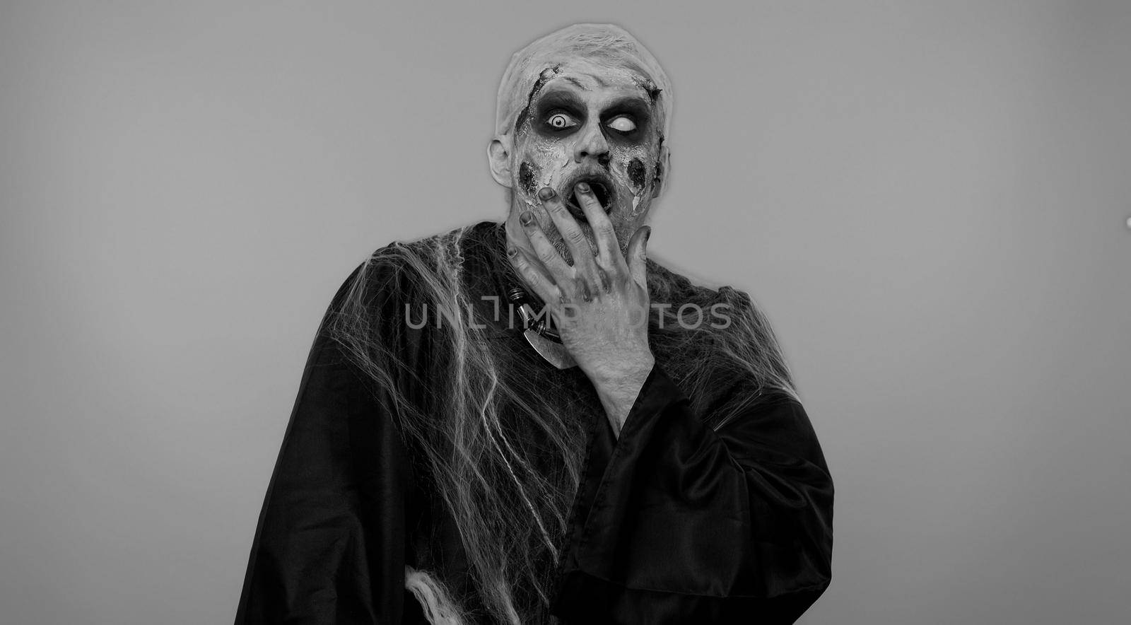 Oh my God, Wow. Frightening man with Halloween zombie bloody wounded makeup raising hands in surprise looking at camera with big eyes, shocked by sudden victory. Excited amazed sinister undead guy
