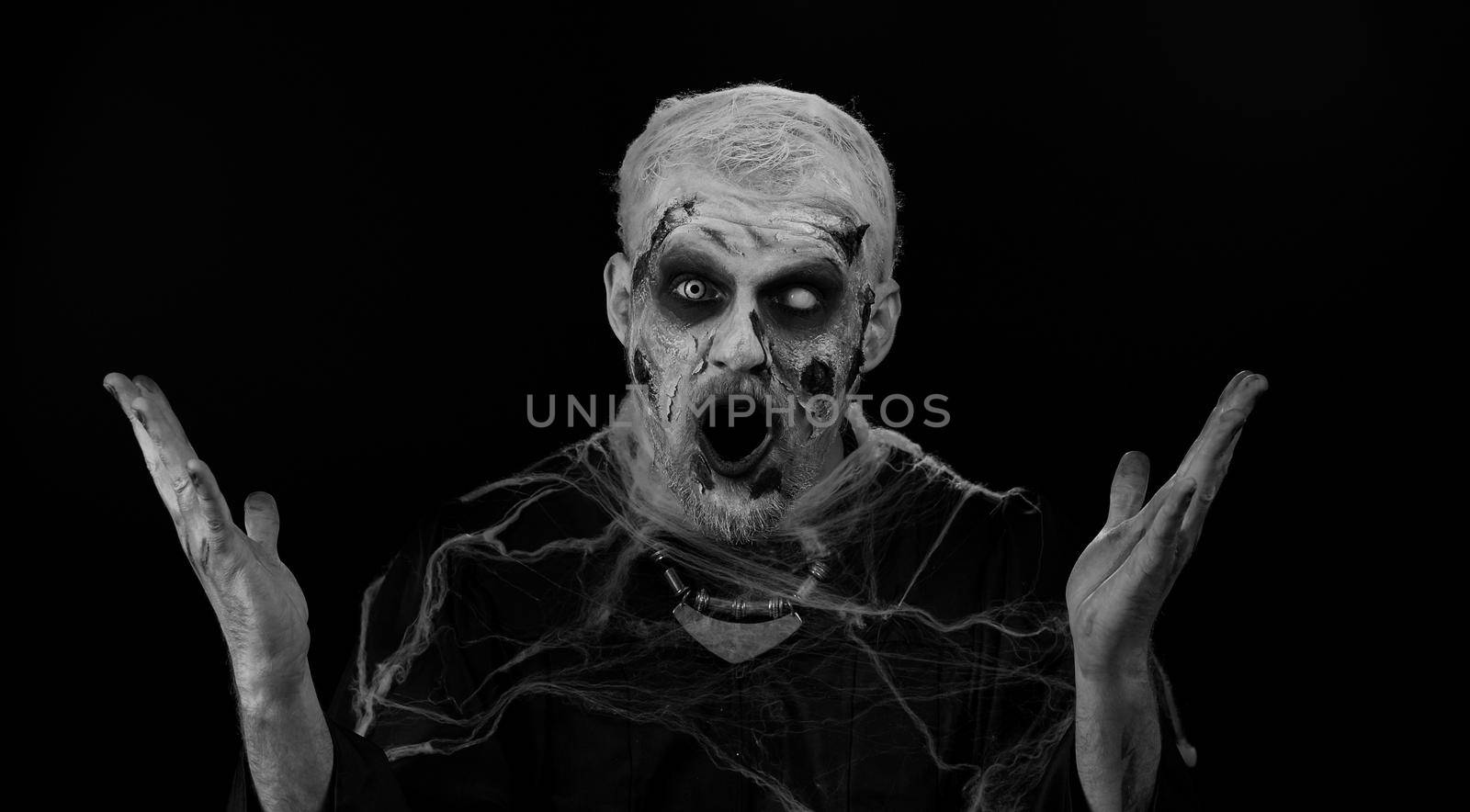 Oh my God, Wow. Scary man alone with Halloween zombie bloody wounded makeup raising hands in surprise looking at camera with big eyes, shocked by sudden victory. Excited amazed sinister undead guy