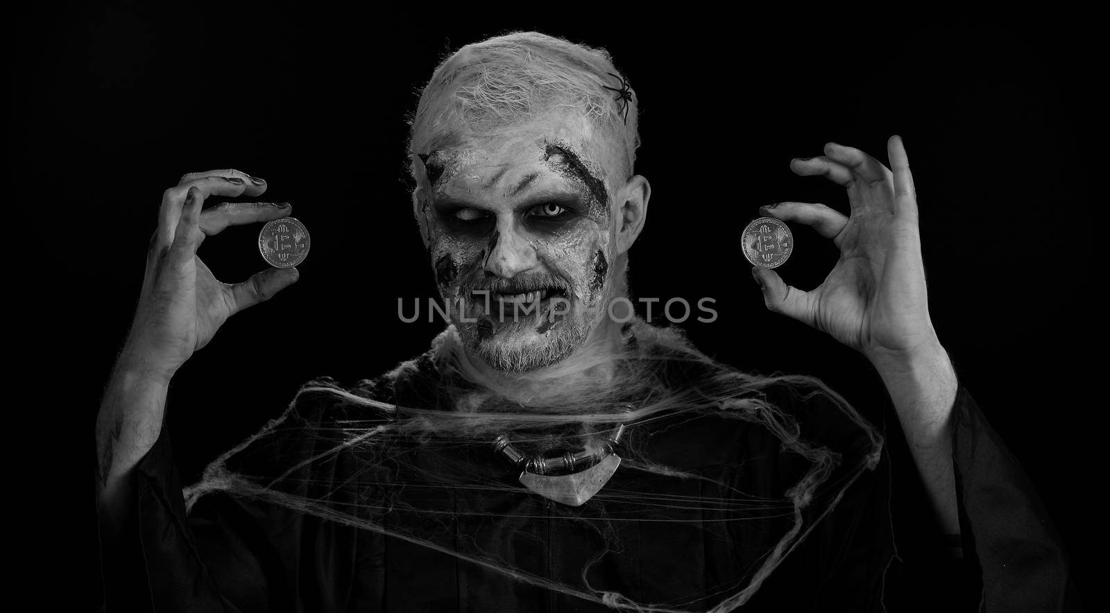 Zombie man with make-up with fake wounds scars showing golden bitcoins. Achievement career wealth, cryptocurrency investment, mining btc, future technology. Sinister dead guy. Halloween, filming
