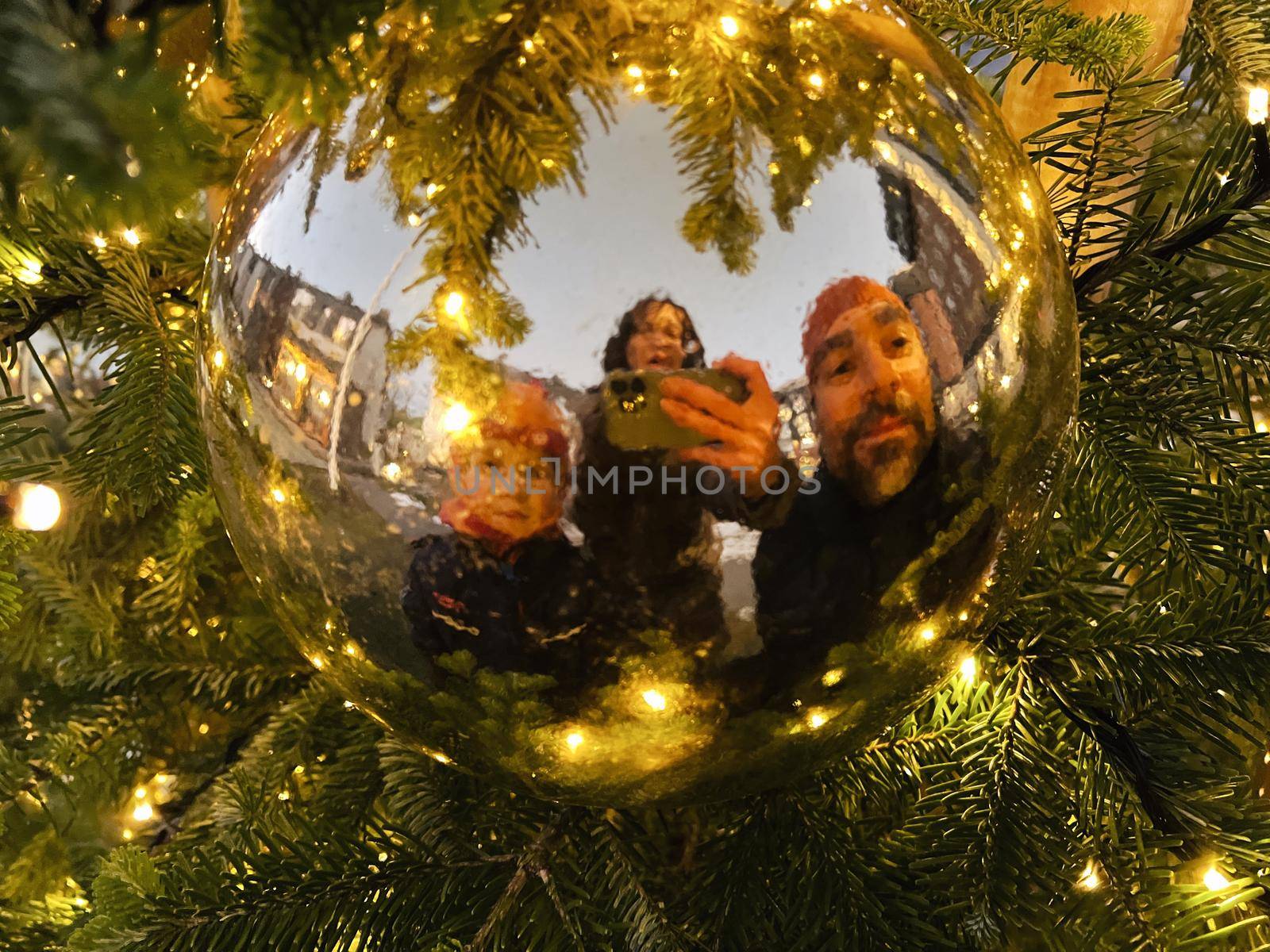 Closeup of a family with one Child looking into a Christmas ball hanging on a Christmas tree with lights