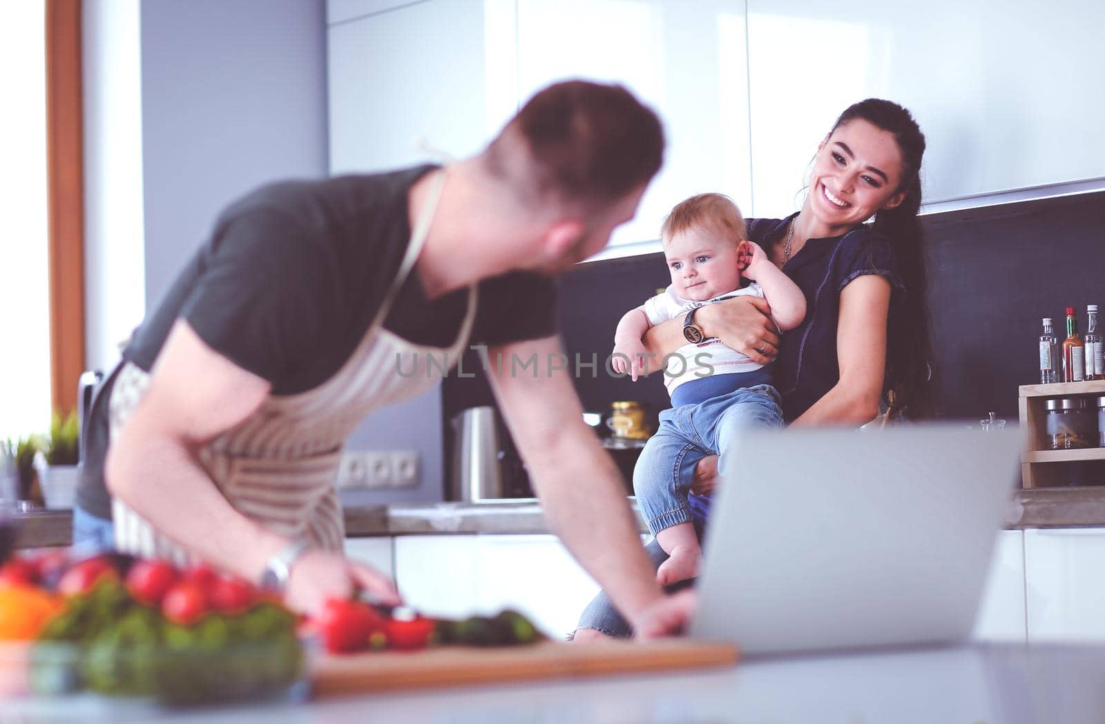 Portrait of man cooking vegetable in the kitchen while looking at a laptop computer on the table.
