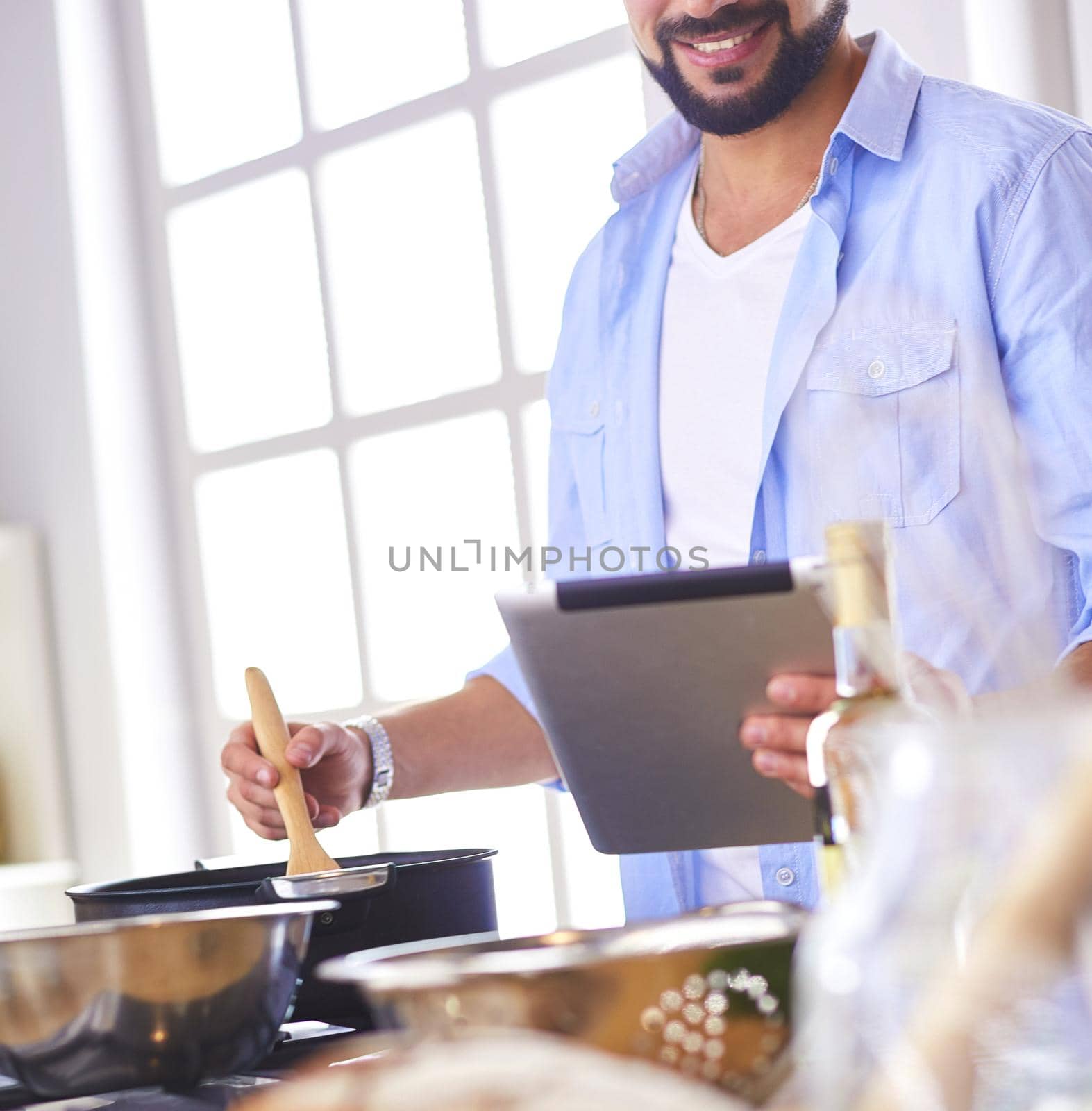 Man following recipe on digital tablet and cooking tasty and healthy food in kitchen at home.